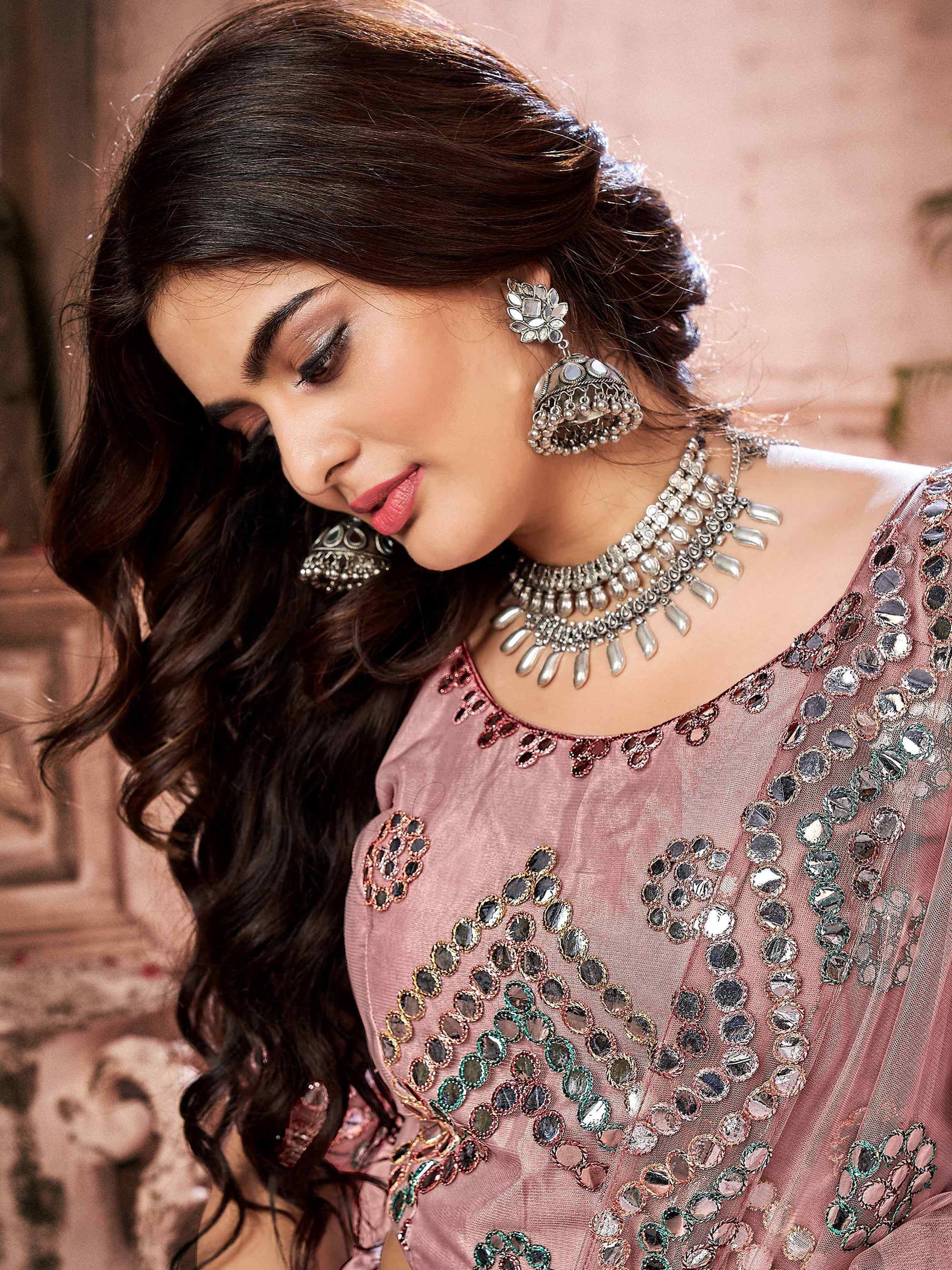 Woman in pink ethnic gown with mirror work, statement jewelry, and traditional Indian attire