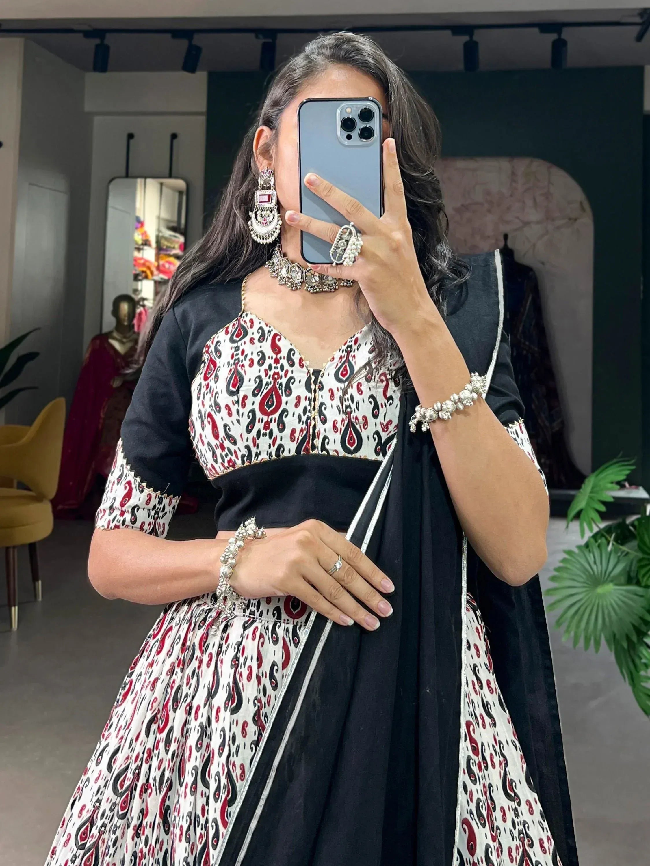 Woman in black and white paisley print lehenga choli with ethnic jewelry, taking mirror selfie