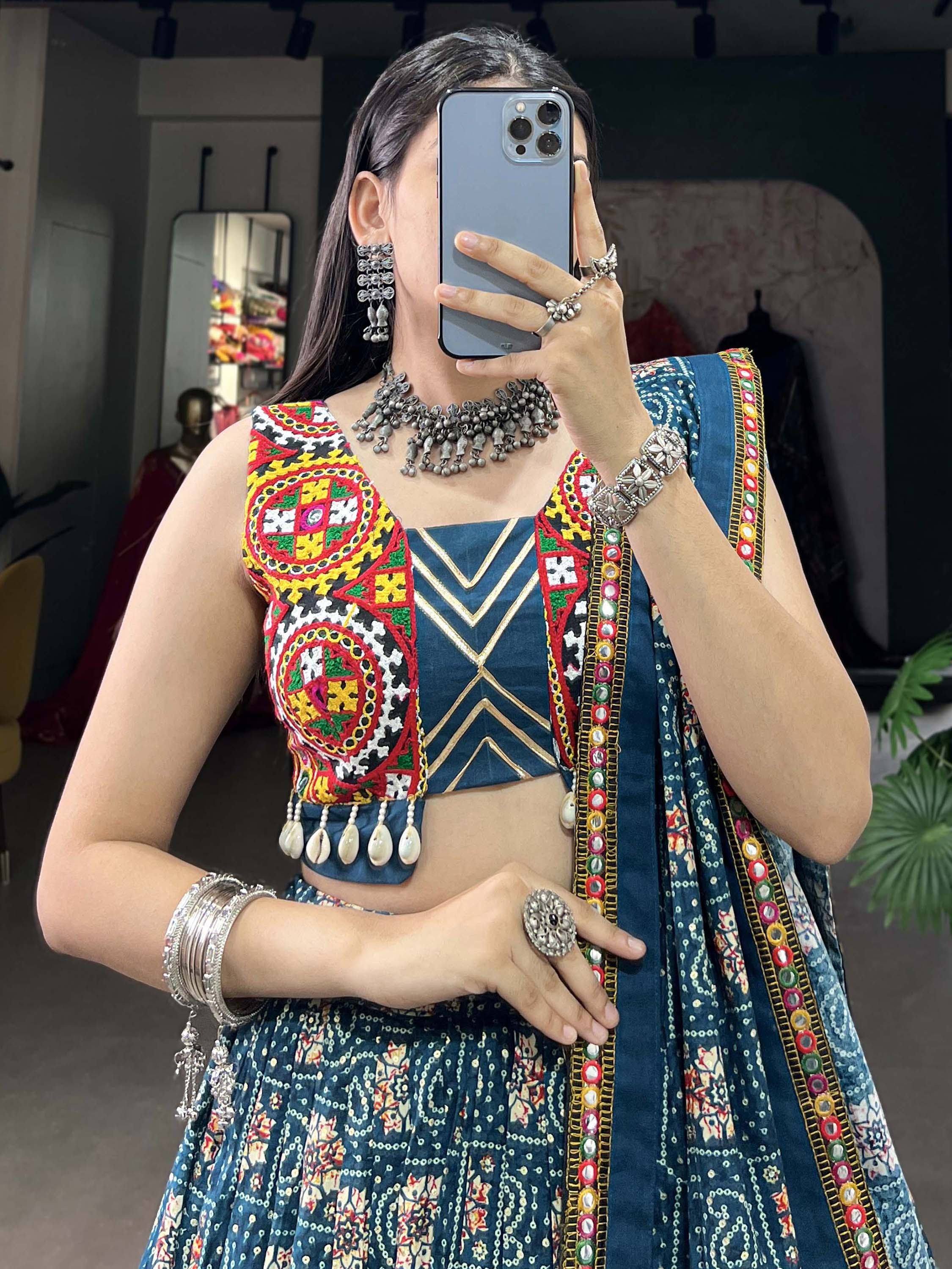 Woman in vibrant blue embroidered lehenga choli with mirror work, traditional jewelry, and mirror selfie