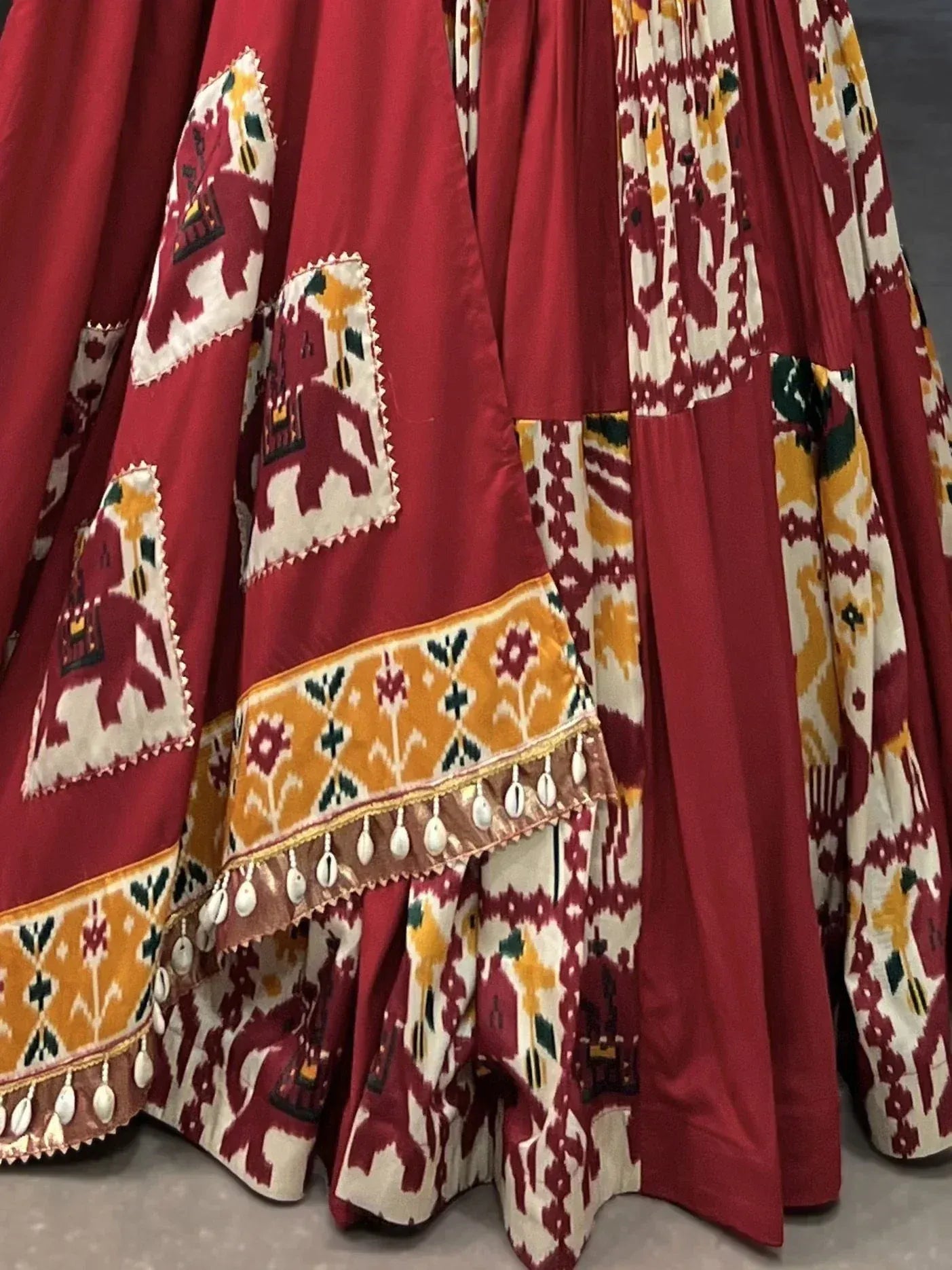 Red ethnic lehenga with elephant print, ikat patterns, and shell tassels for festive occasions