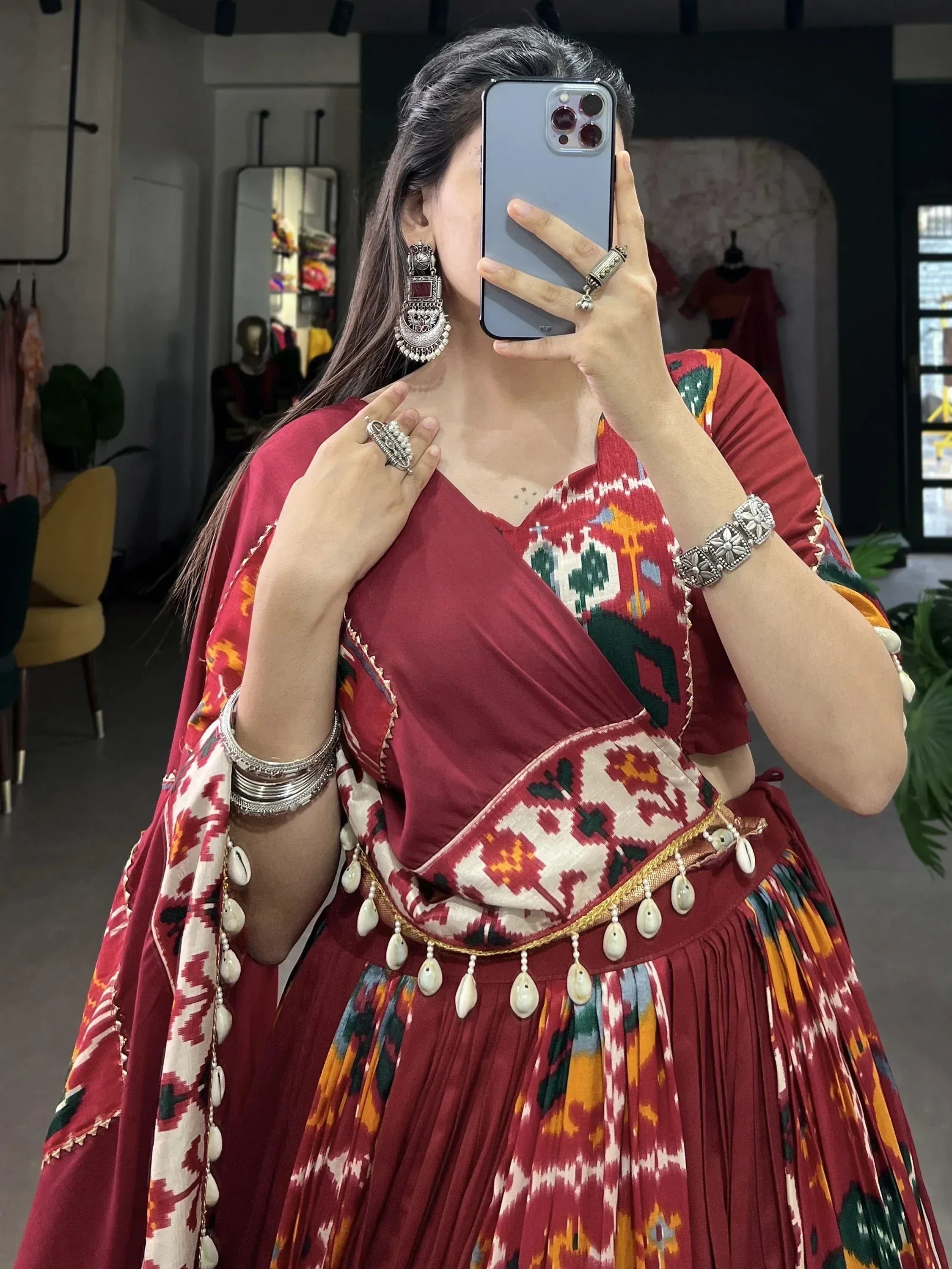 Woman in maroon ikat print ethnic lehenga choli with silver jewelry, mirror selfie in boutique