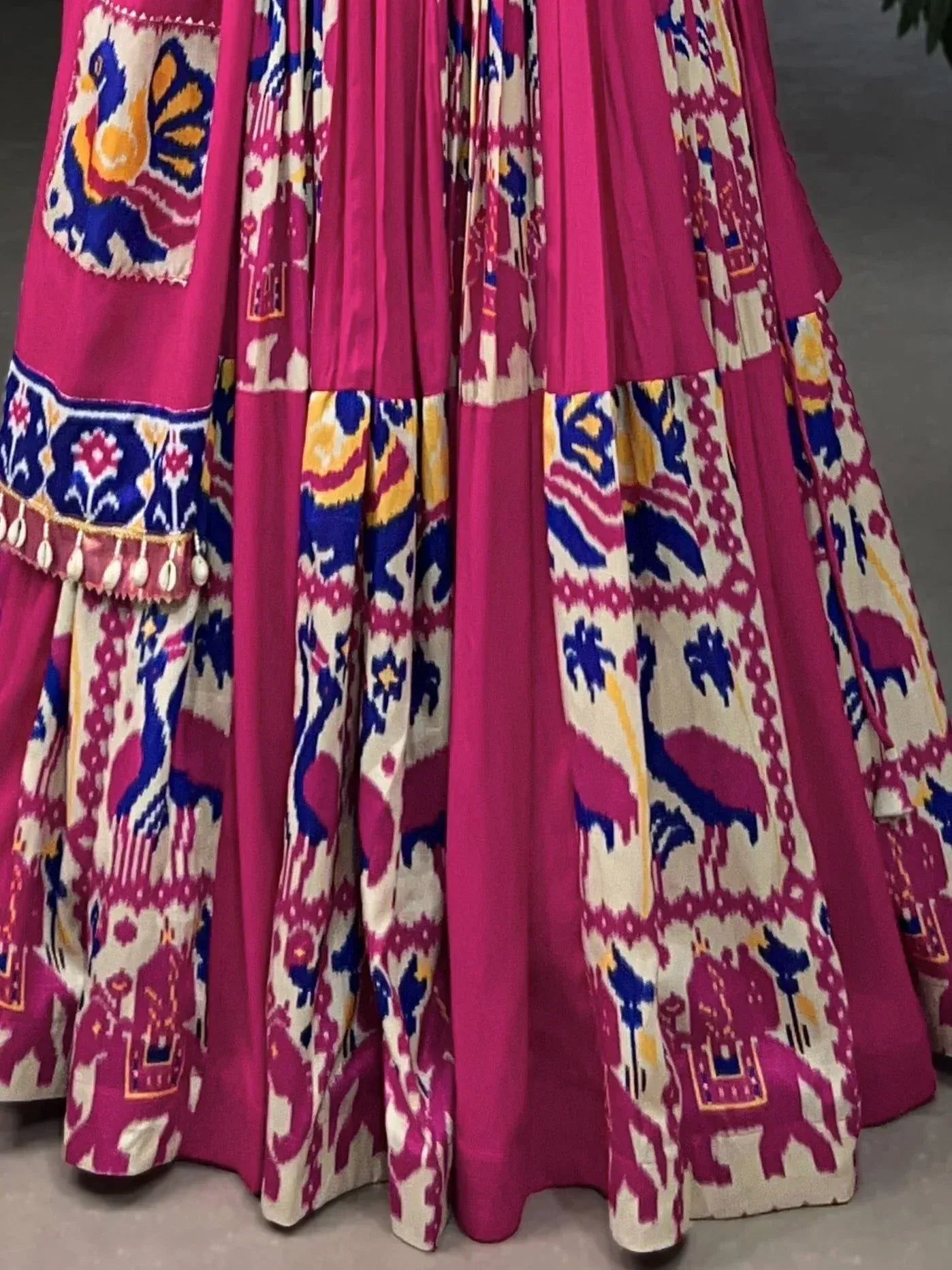 Vibrant pink ethnic lehenga with blue and yellow Ikat print, elephant motifs, and shell tassels
