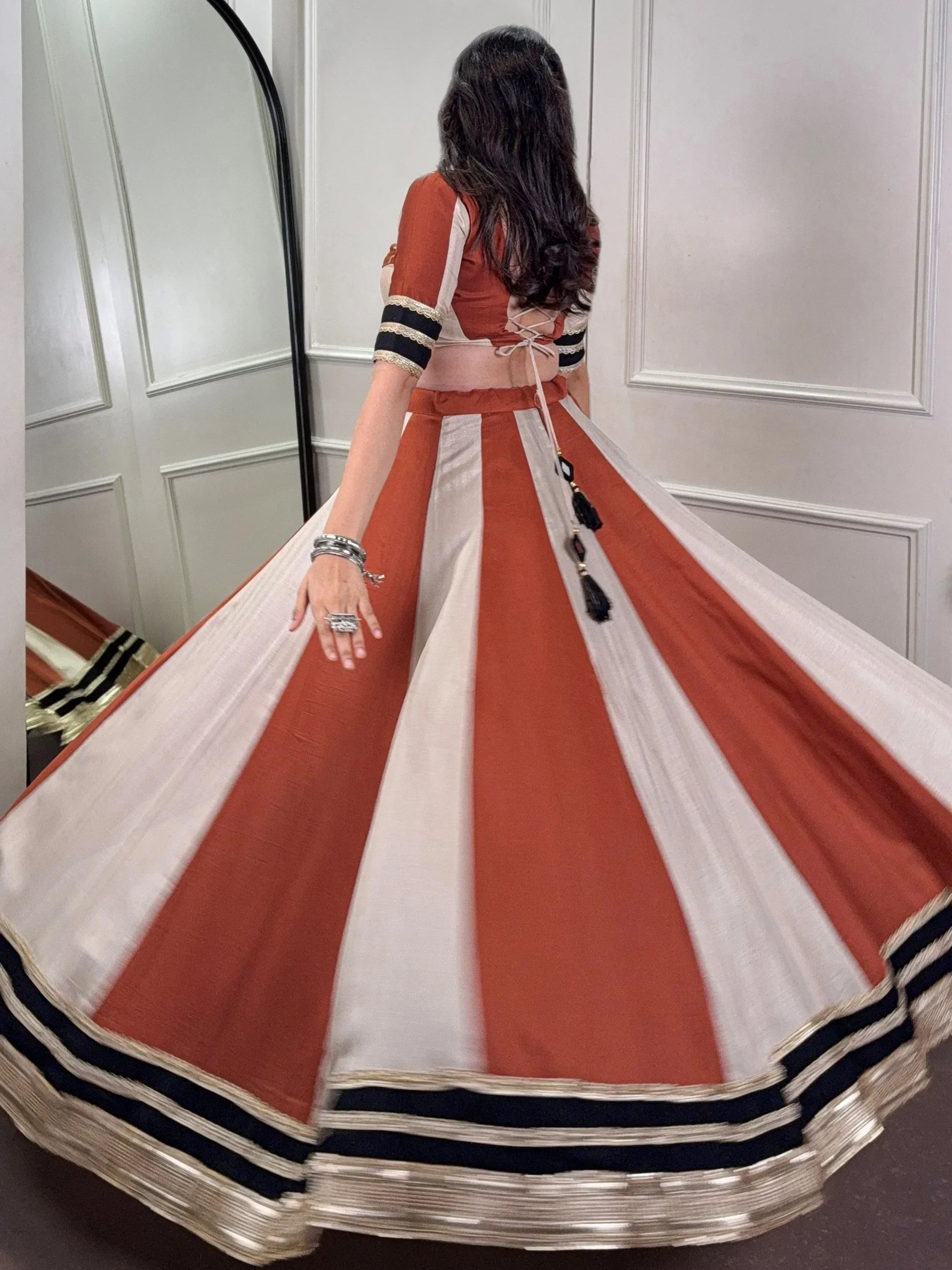 Woman in orange and white striped lehenga choli with black border, back view