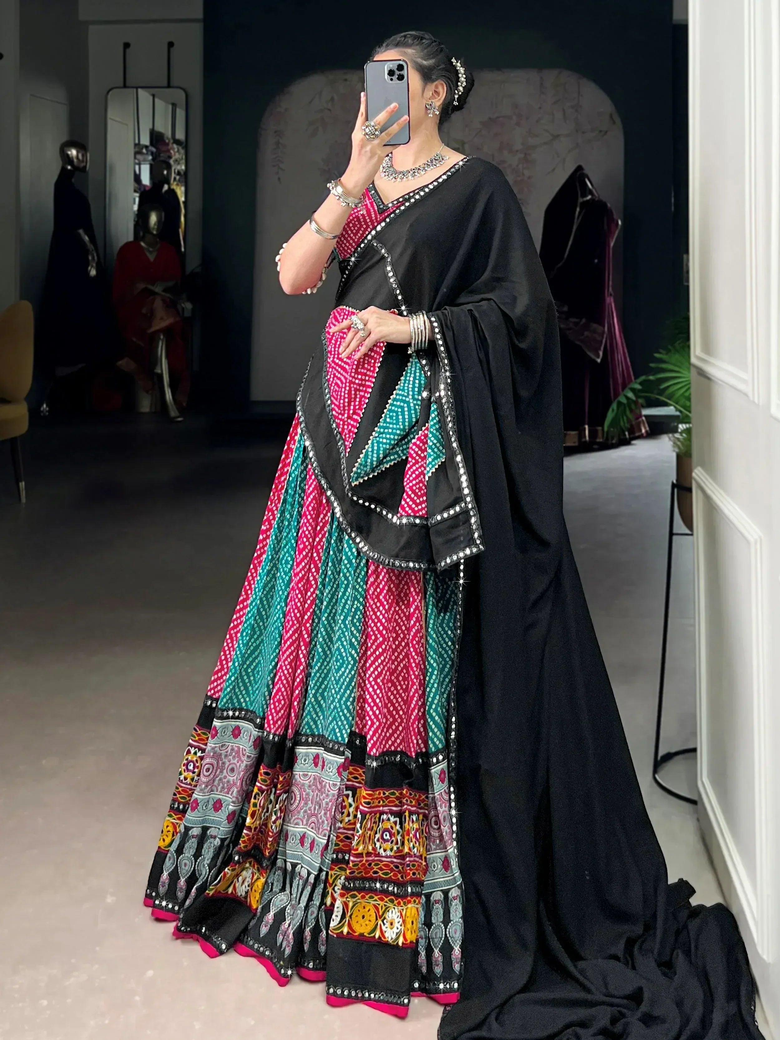 Black ethnic lehenga choli with pink and teal printed skirt, mirror work, and statement jewelry
