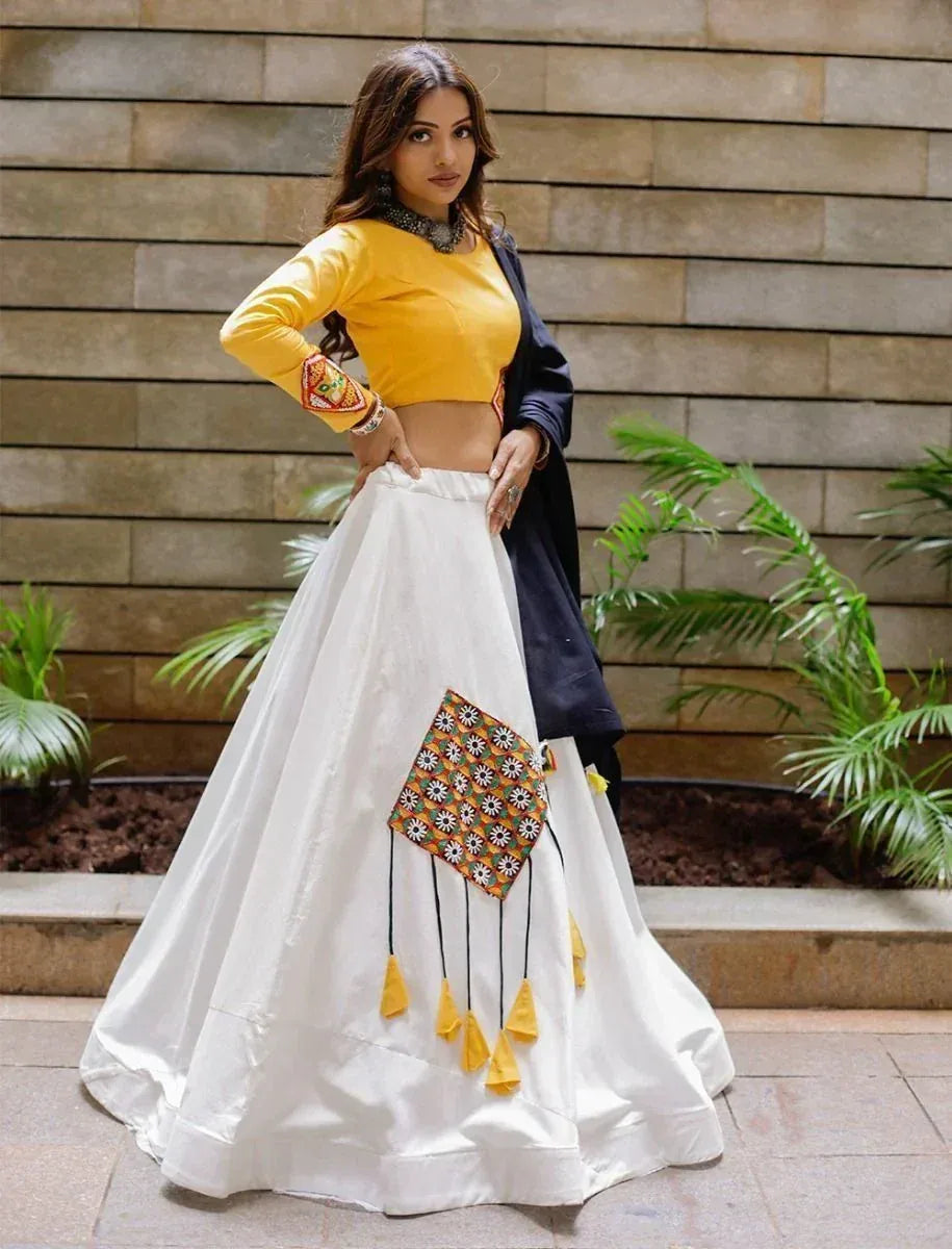Yellow crop top with white lehenga featuring floral embroidery and tassels, styled for ethnic wear.