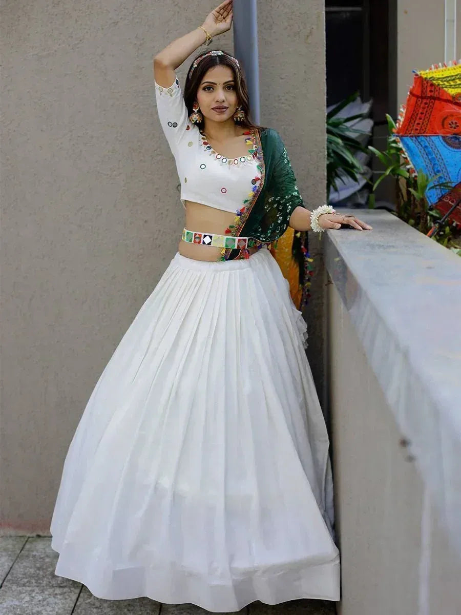 White lehenga choli with colorful mirror work, green dupatta, and floral accessories for Indian ethnic wear
