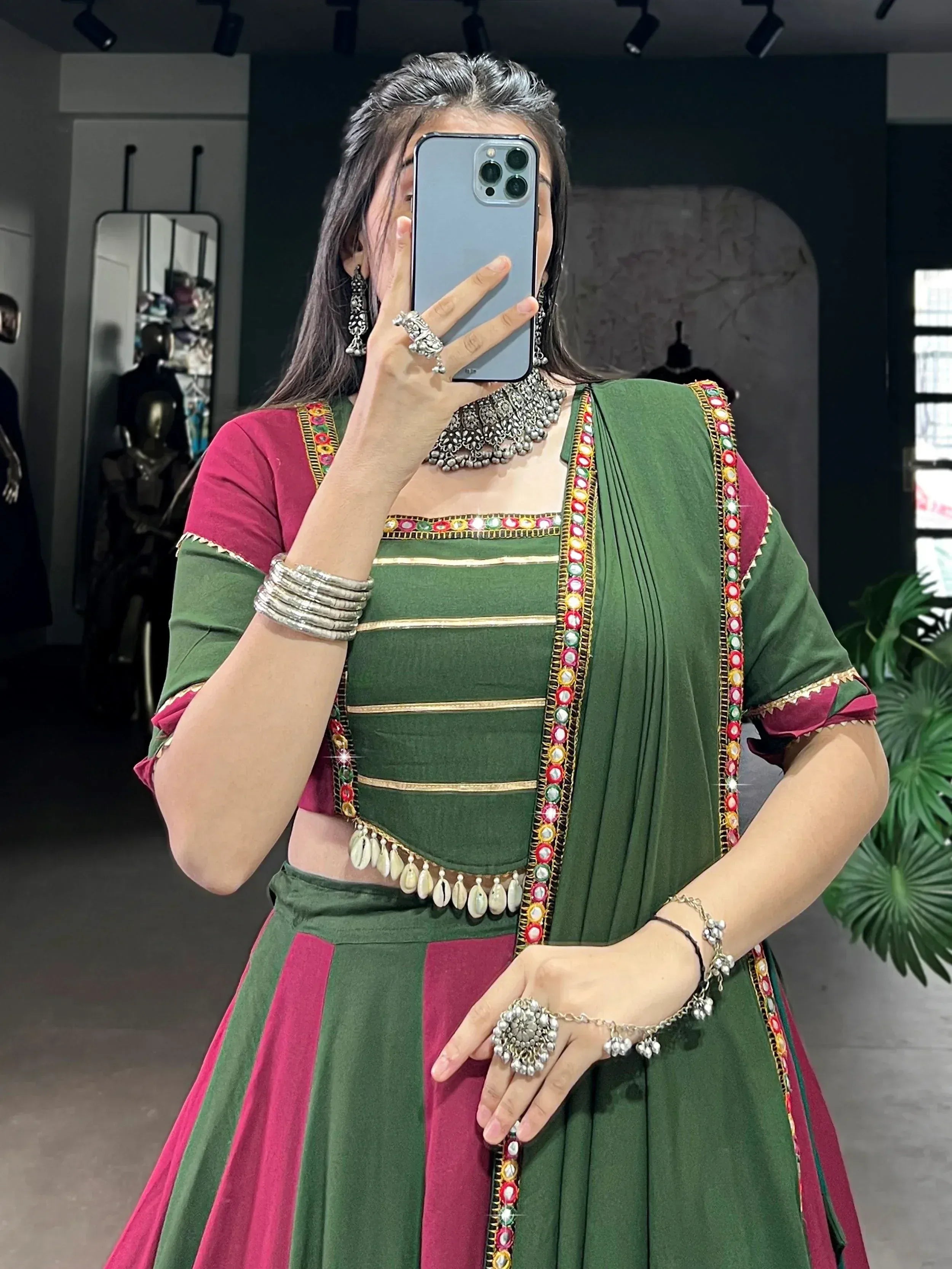 Green and pink ethnic lehenga choli with mirror work and traditional jewelry, perfect for festive occasions.
