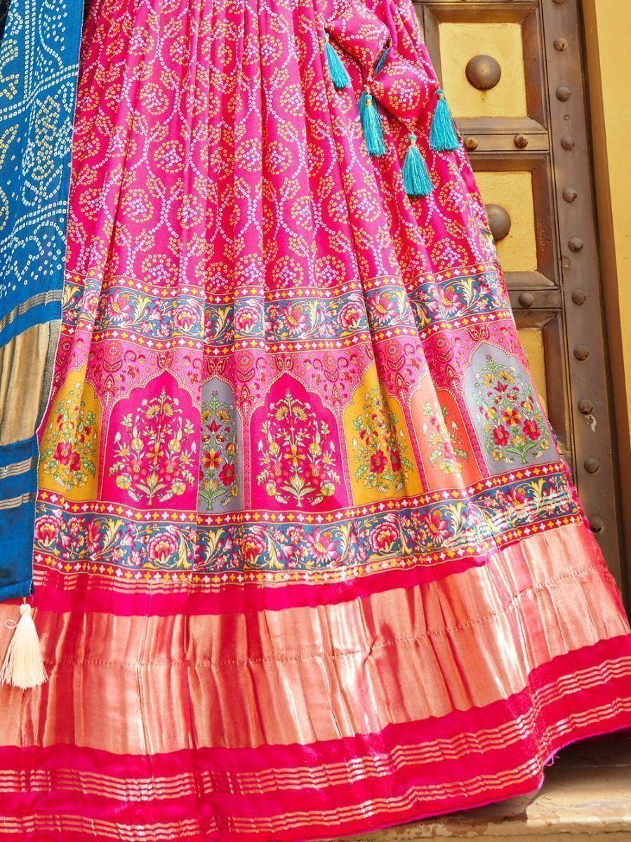 Vibrant pink lehenga with floral embroidery, tassels, and mirror work, paired with blue dupatta for Indian ethnic wear.