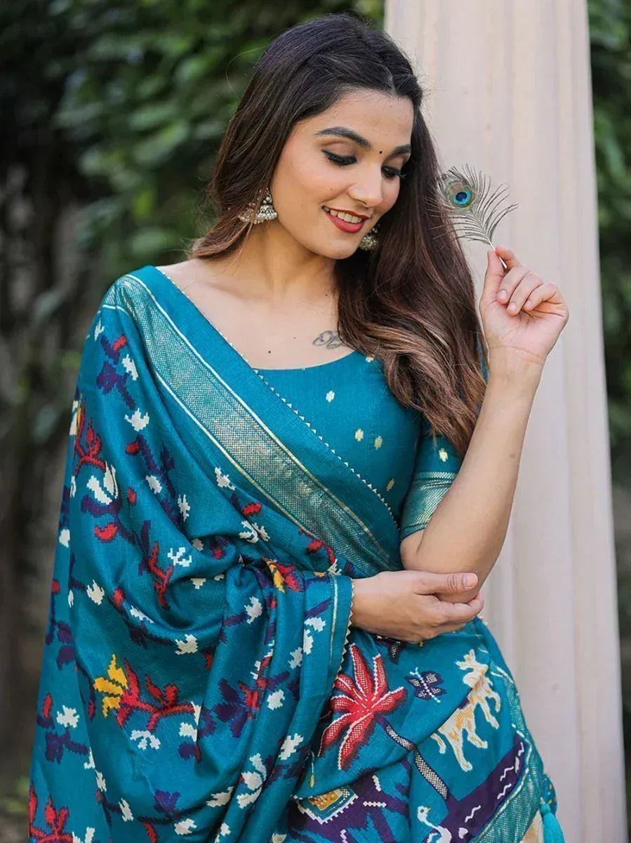 Teal printed saree with floral and animal motifs, paired with blouse, held with peacock feather