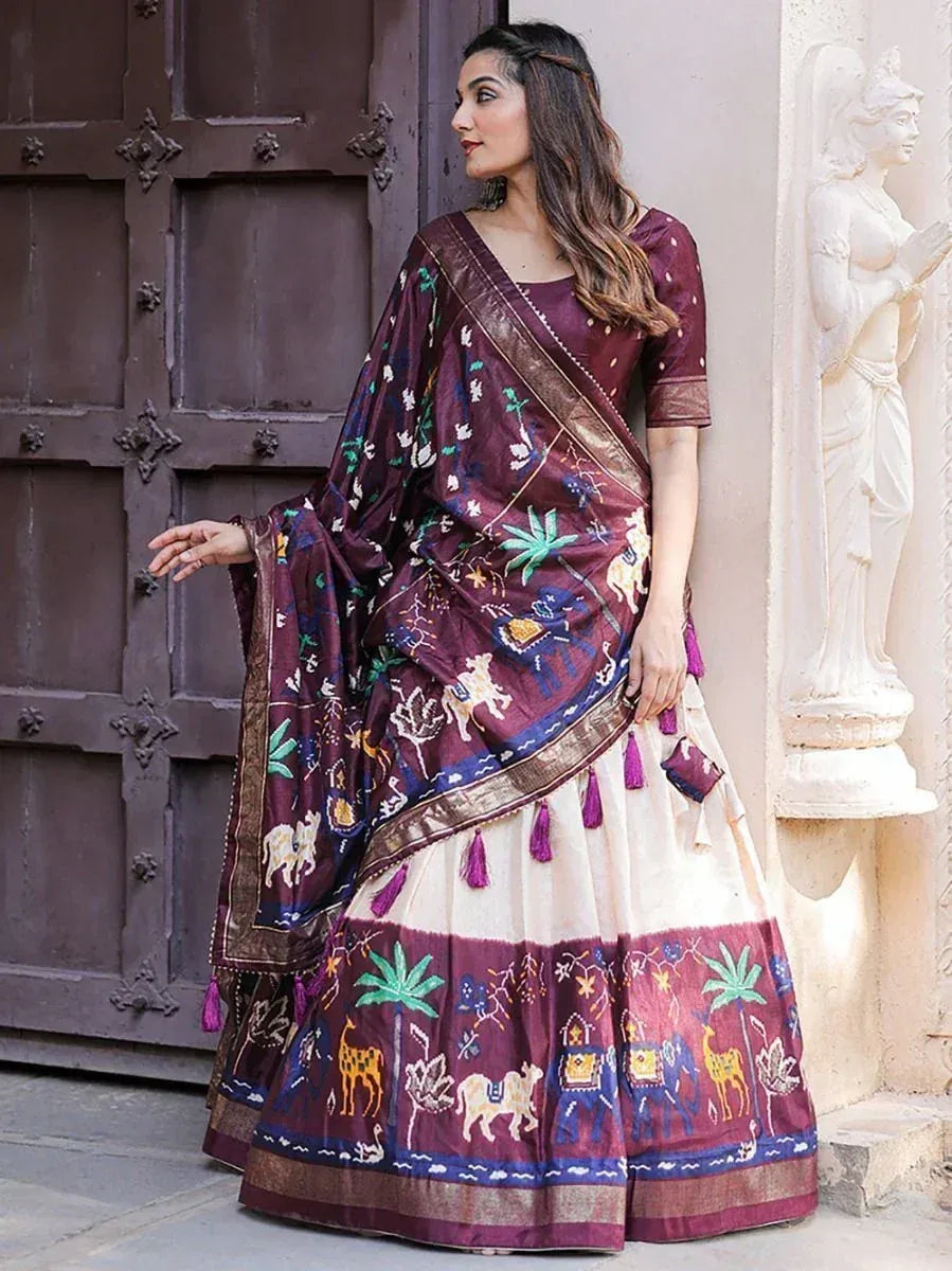 Woman in maroon and cream embroidered lehenga choli with animal motifs, standing by carved door and statue