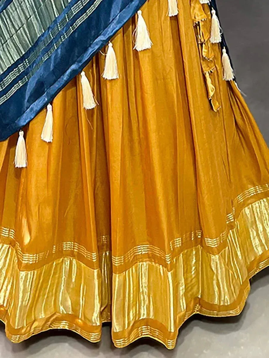 Mustard yellow lehenga with gold trim and white tassels, paired with blue dupatta for ethnic wear