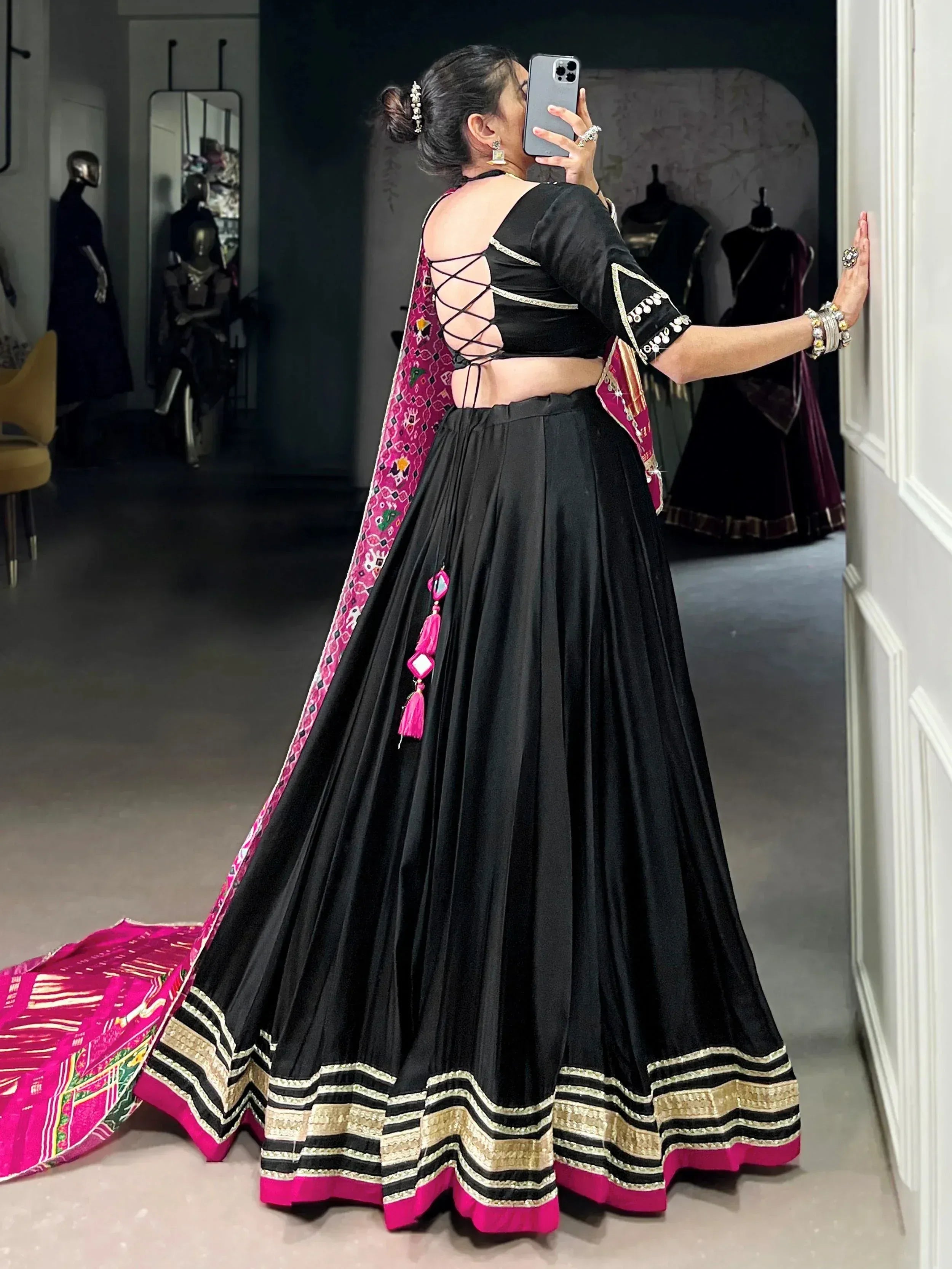 Black lehenga choli with pink embroidery and gold border, back view with crisscross blouse design