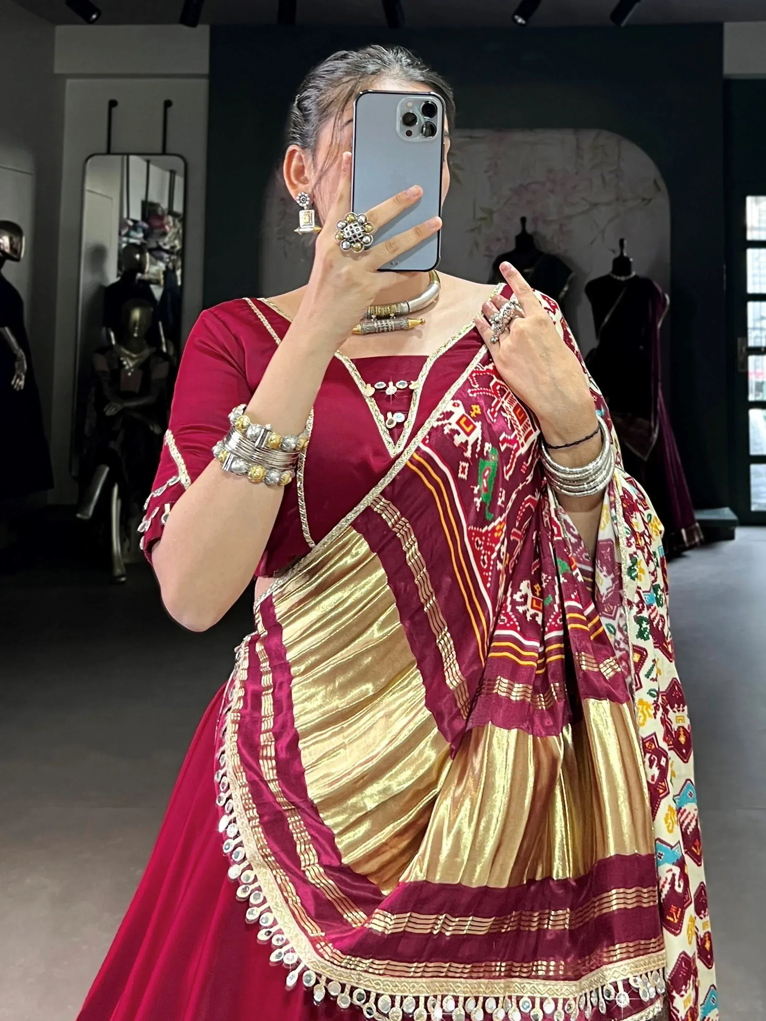 Woman in maroon and gold ethnic lehenga choli with mirror work, taking mirror selfie in boutique