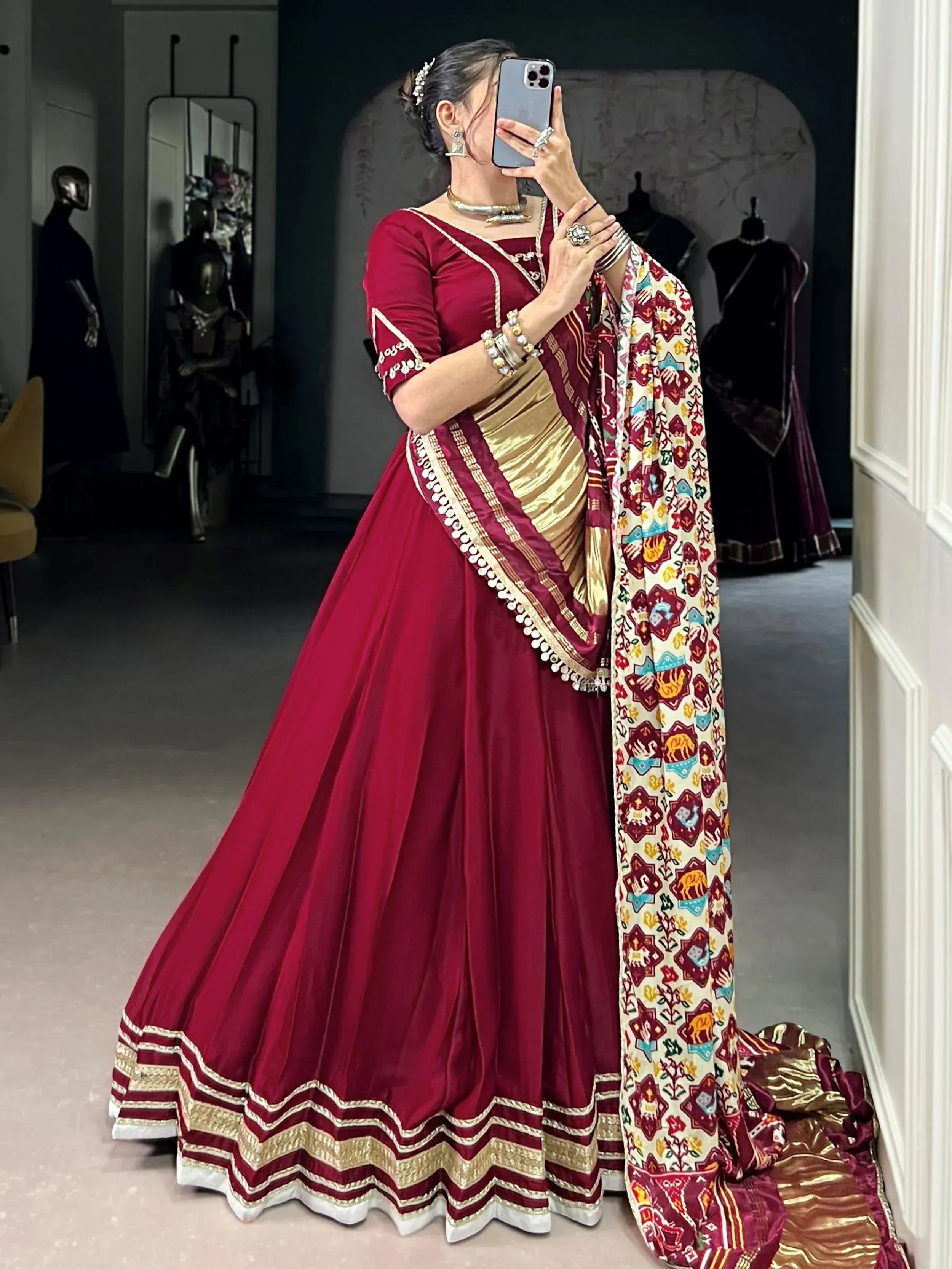 Woman in maroon designer lehenga choli with gold embroidery and printed dupatta, taking mirror selfie