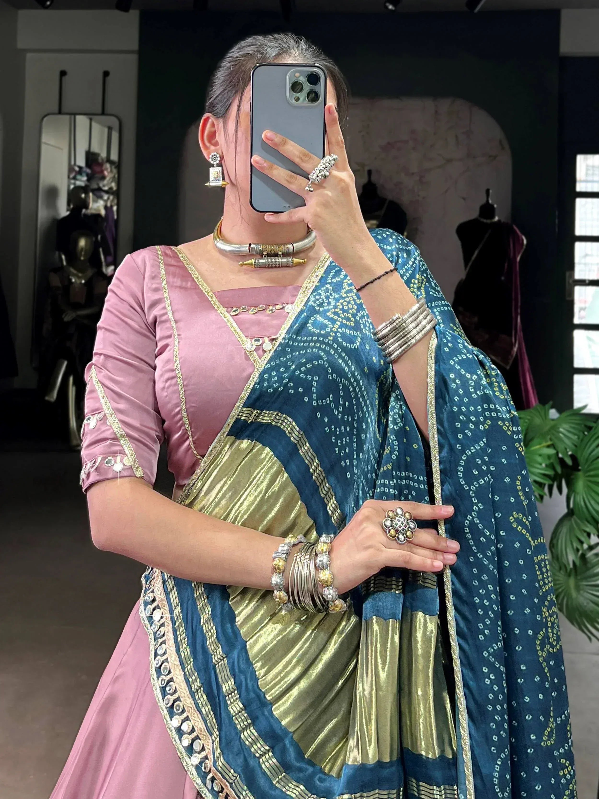 Woman in pink blouse and blue-gold patterned saree with traditional Indian jewelry, taking mirror selfie