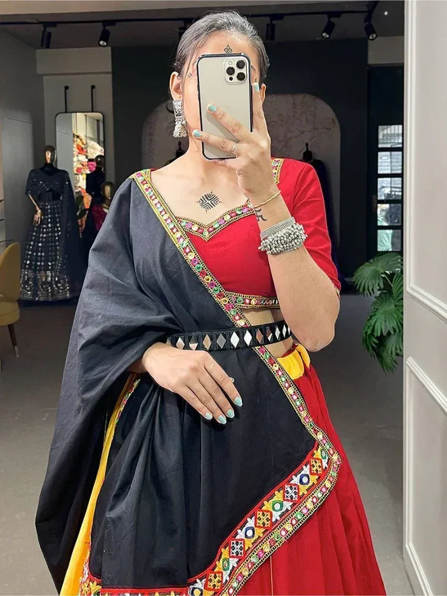Woman wearing red and black embroidered lehenga choli with mirror work, taking mirror selfie in boutique