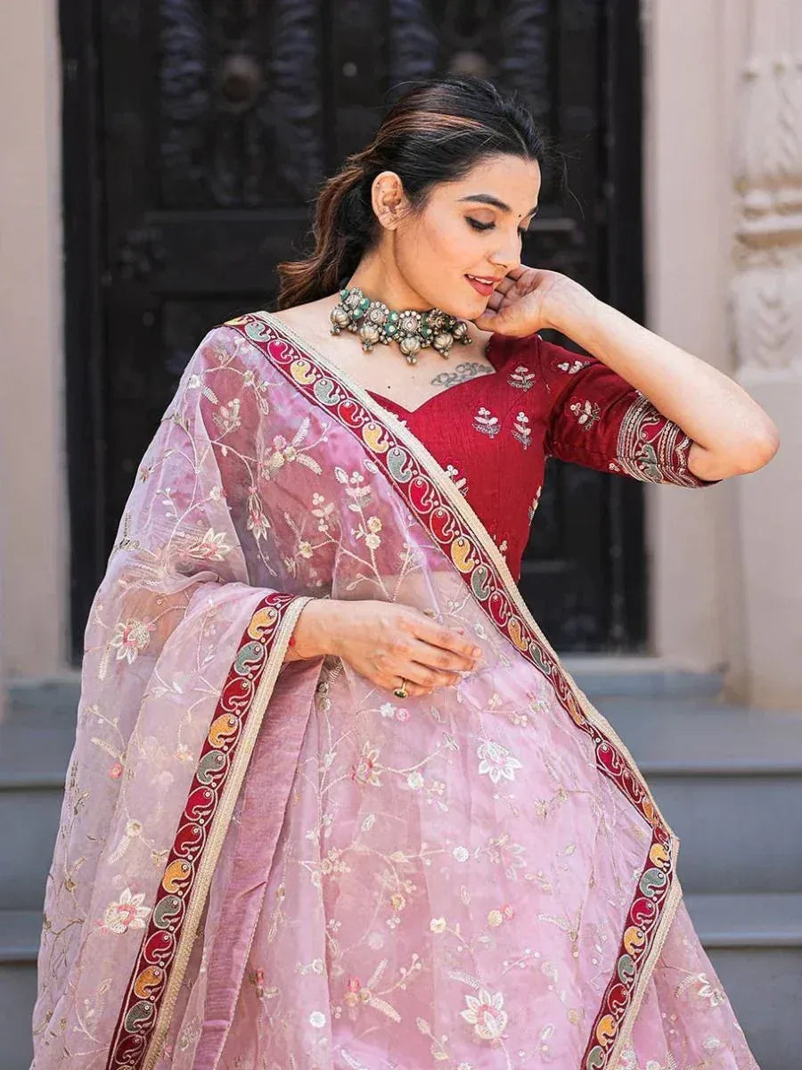Pink embroidered lehenga choli with red blouse, floral detailing, and traditional jewelry for Indian ethnic wear