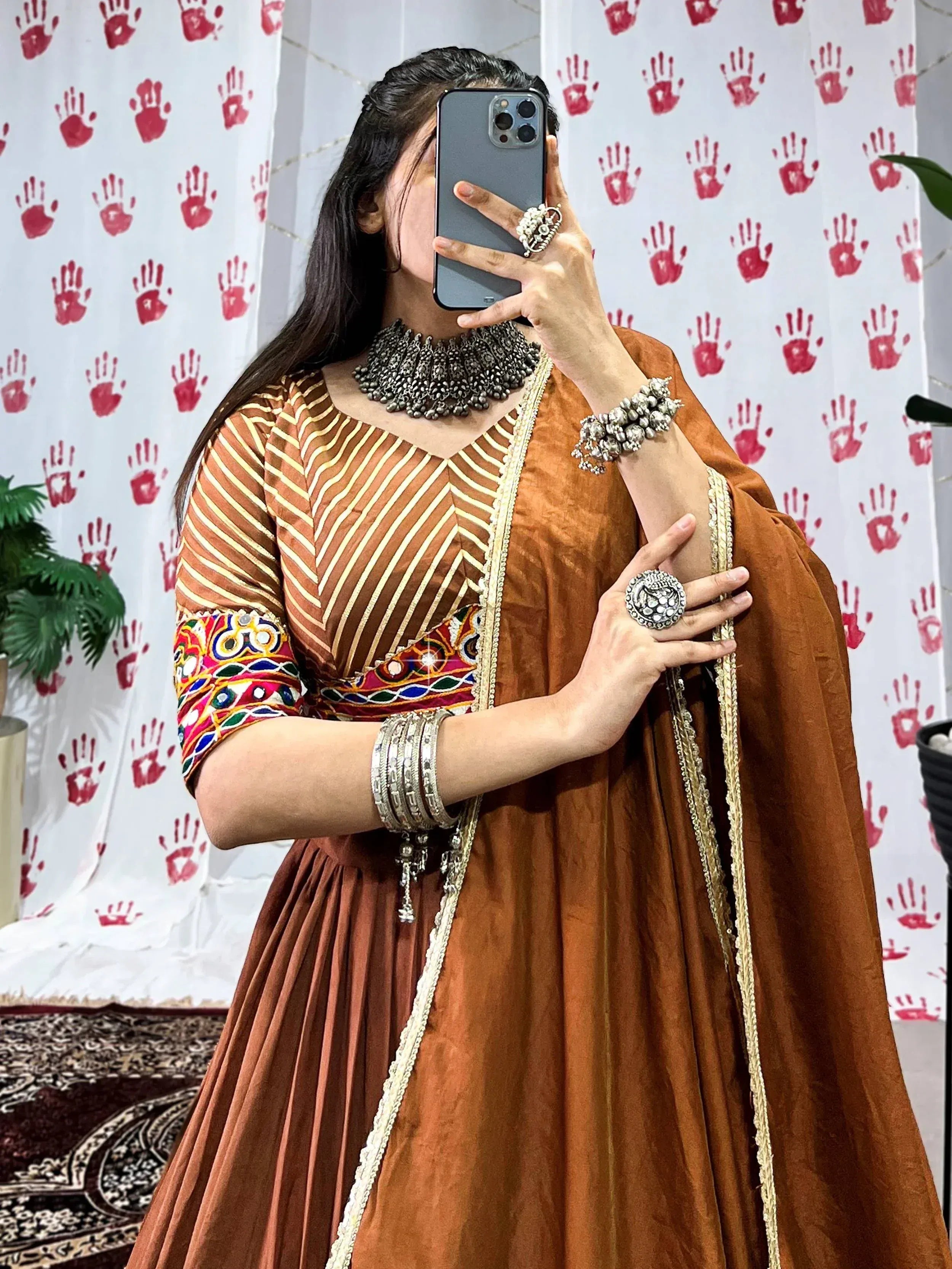Woman in rust ethnic gown with mirror work, gold trim, and silver jewelry, taking mirror selfie