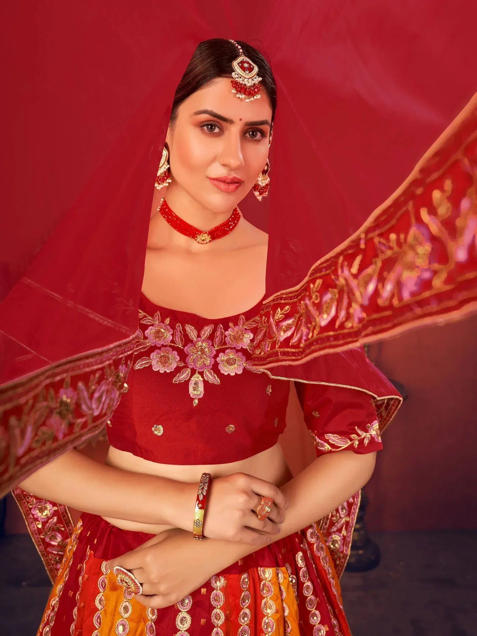 Red embroidered lehenga choli with floral motifs, matching dupatta, and traditional Indian jewelry for festive occasions