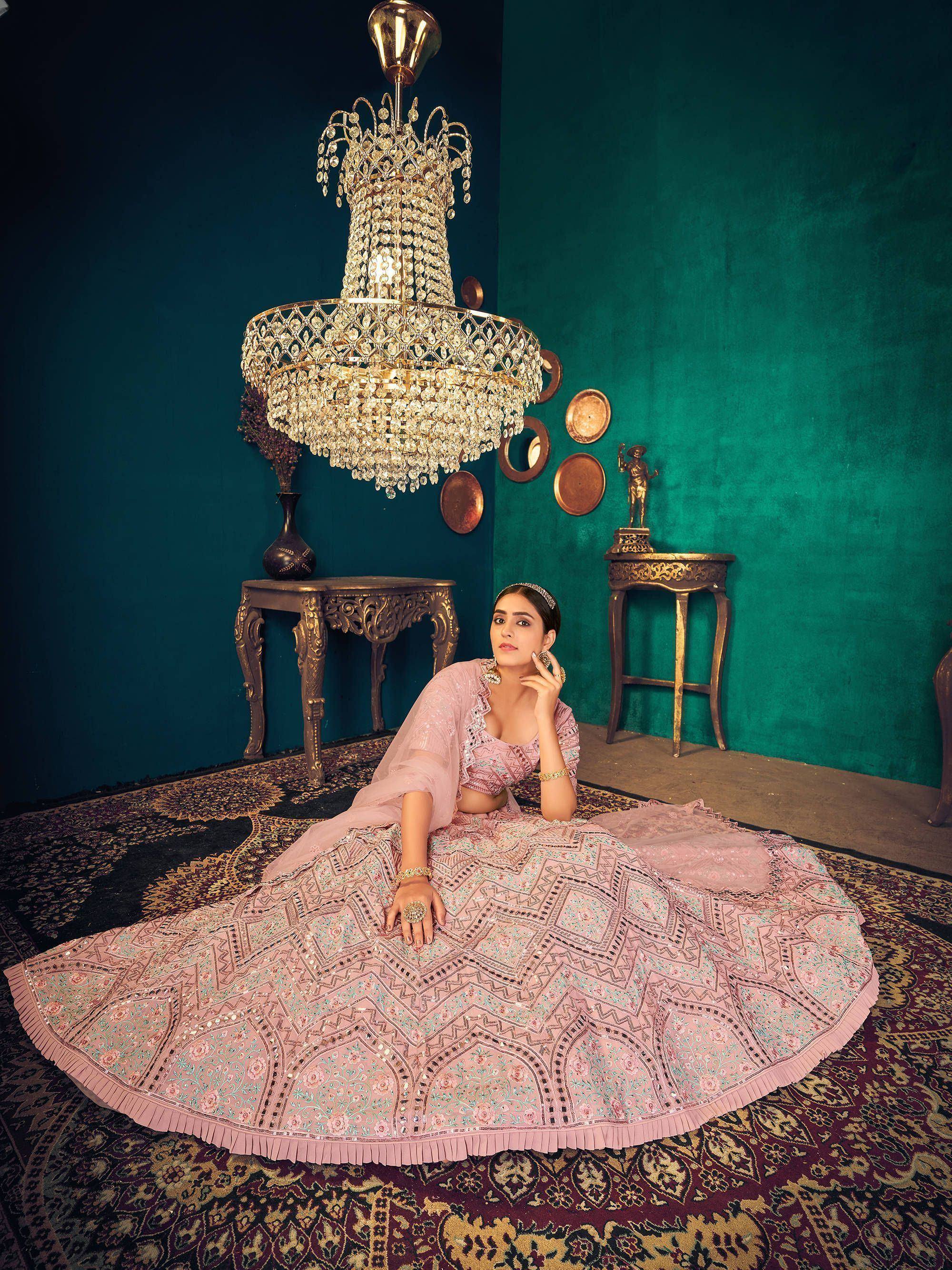 Elegant pink embroidered lehenga choli with intricate patterns, styled under a crystal chandelier.