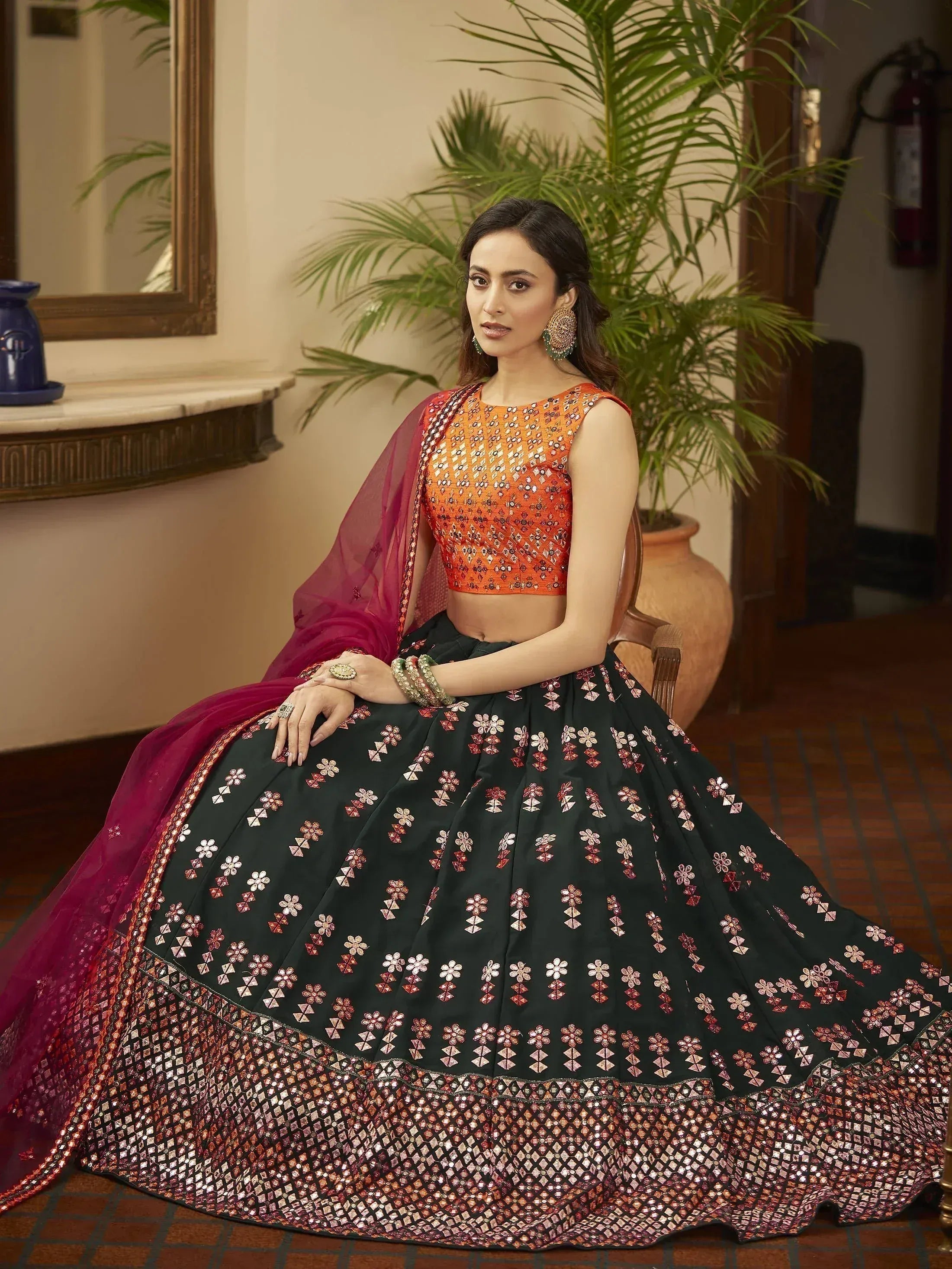 Woman in designer lehenga choli with orange blouse, black skirt, and maroon dupatta, perfect for Indian ethnic wear events.