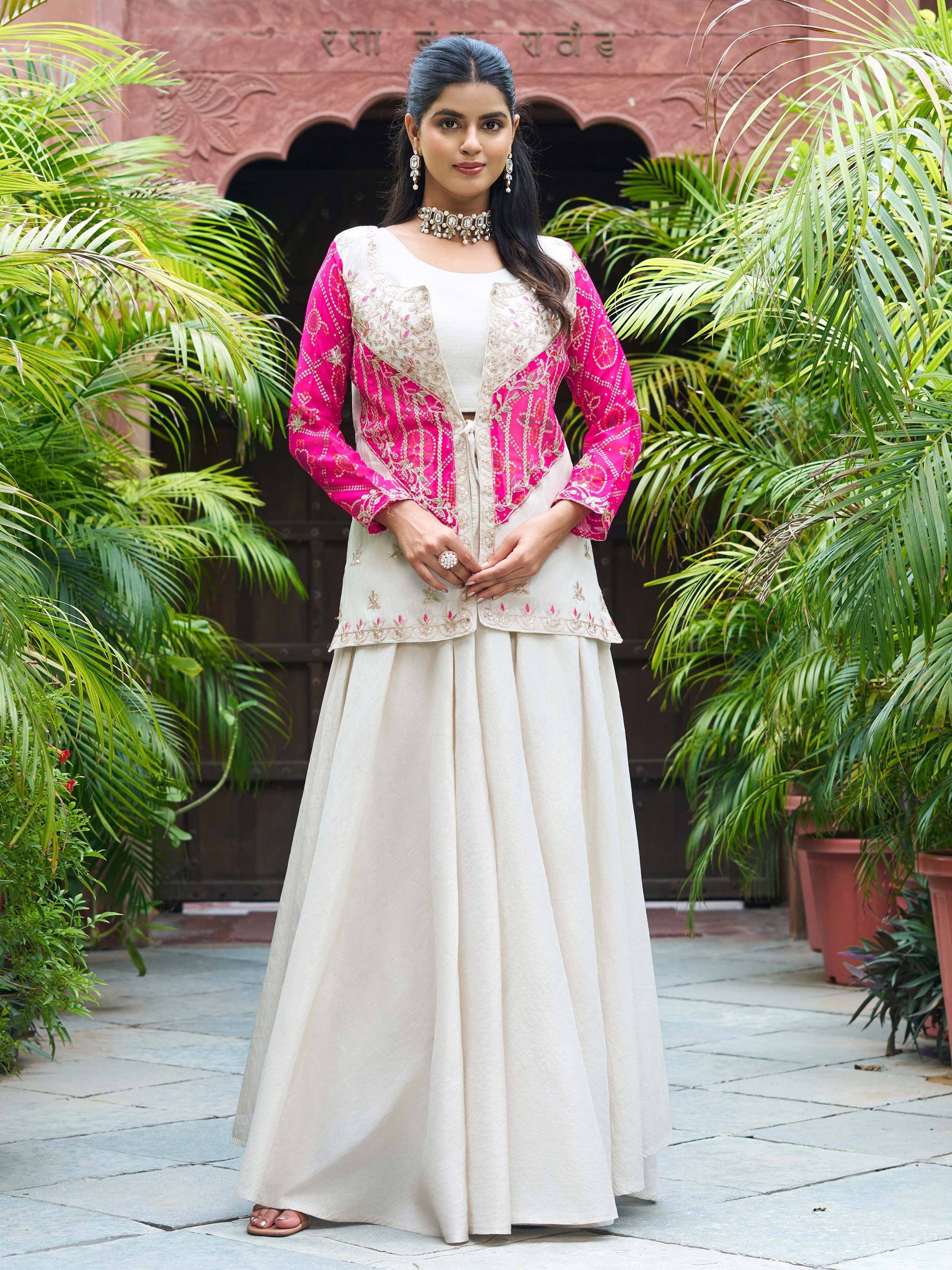 Woman in ivory and pink embroidered ethnic gown with floral patterns, standing outdoors near greenery