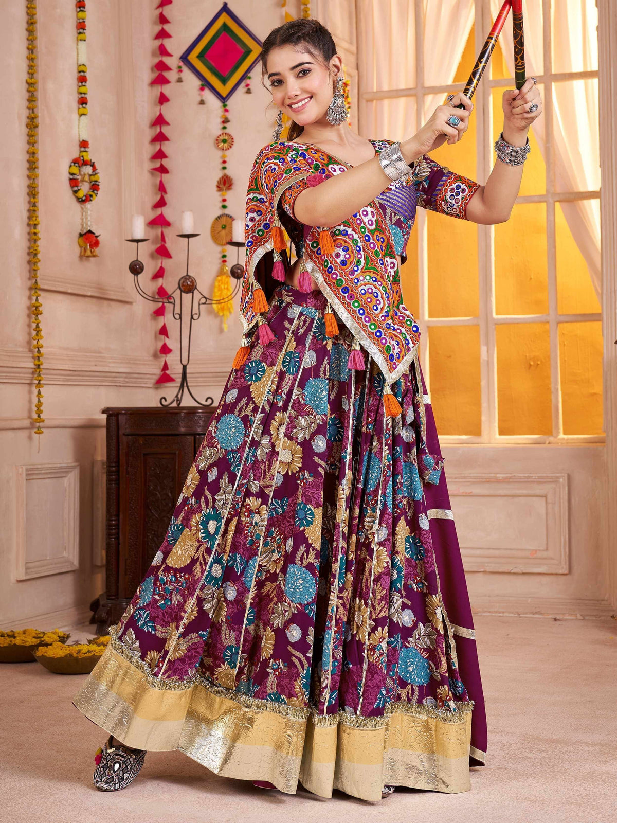 Woman in vibrant purple floral lehenga choli with embroidered dupatta, holding dandiya sticks for festive celebration
