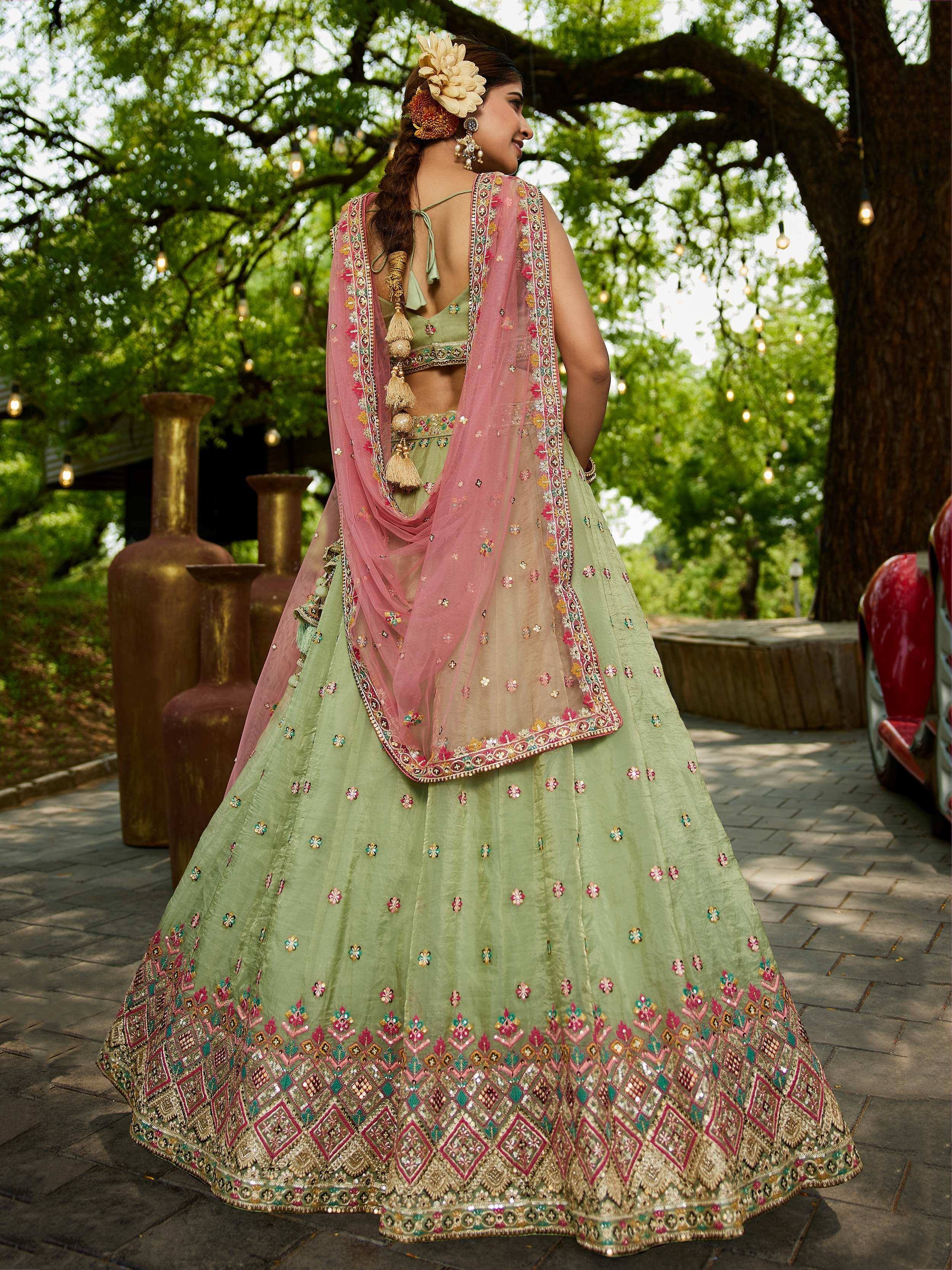 Green embroidered lehenga choli with pink dupatta, floral hair accessory, outdoor garden setting