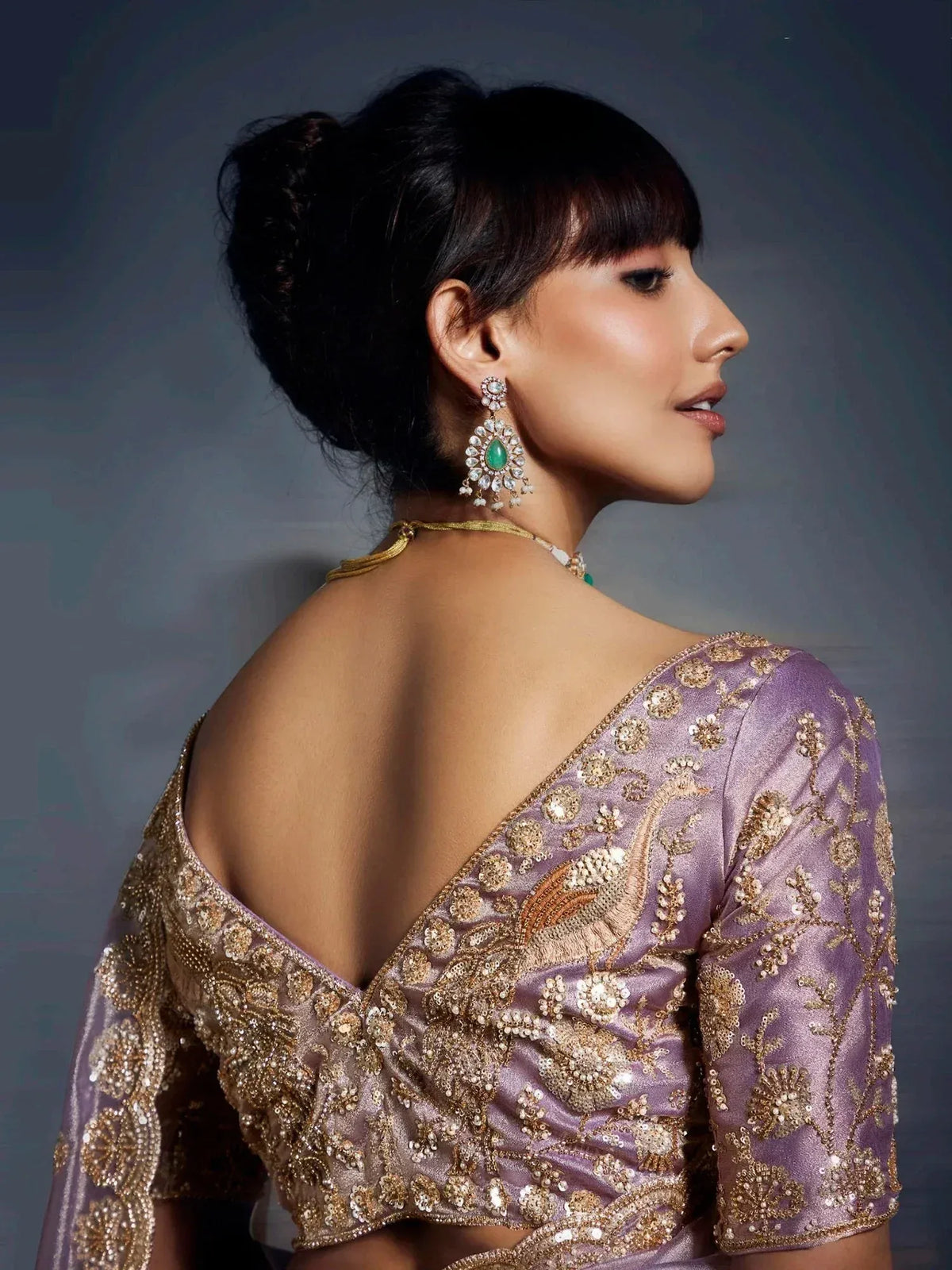 Elegant purple lehenga choli with gold embroidery and backless design, paired with emerald earrings.