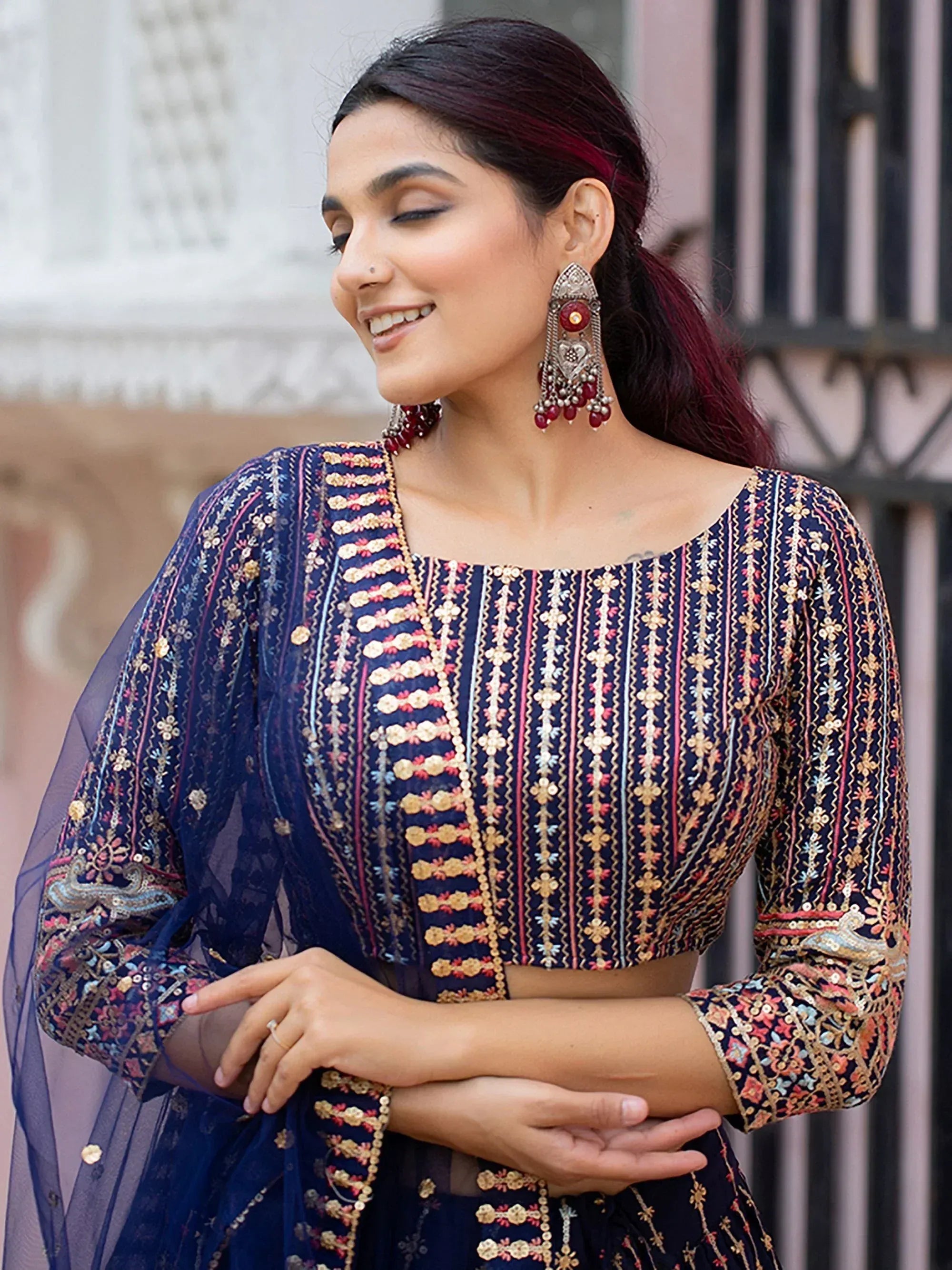 Woman in navy blue embroidered ethnic crop top with gold and pink detailing, paired with statement earrings
