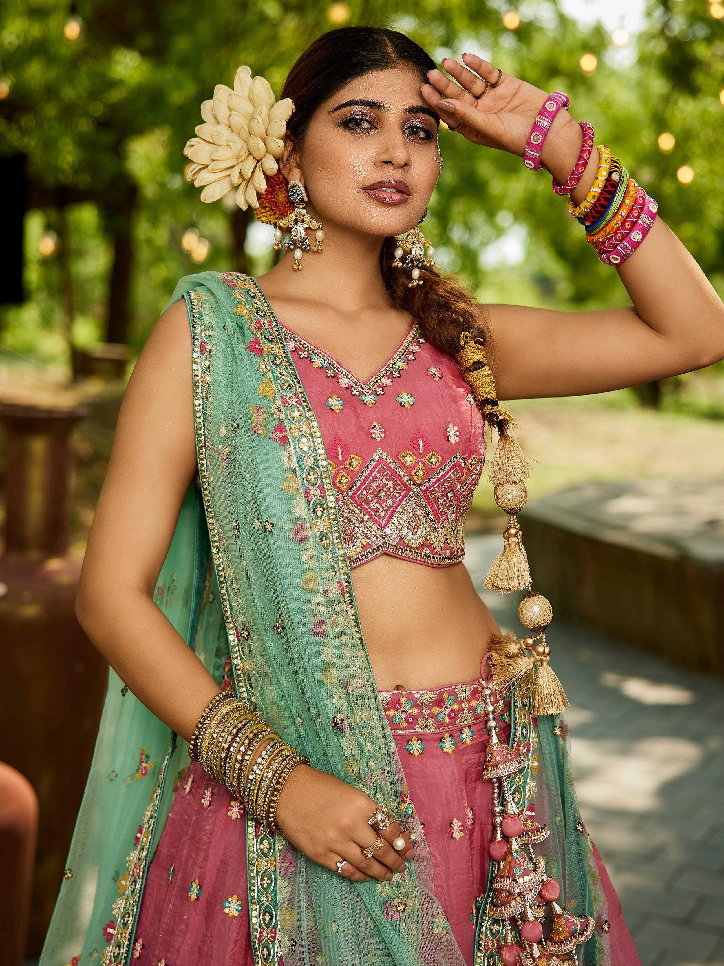 Woman in pink embroidered lehenga choli with green dupatta, floral hair accessory, and traditional jewelry
