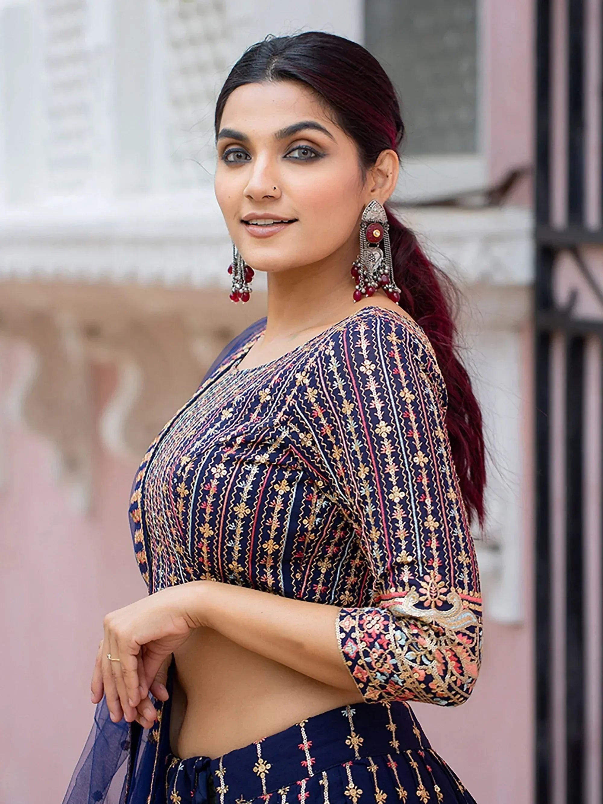Woman in navy blue embroidered lehenga choli with gold and pink detailing, paired with statement earrings