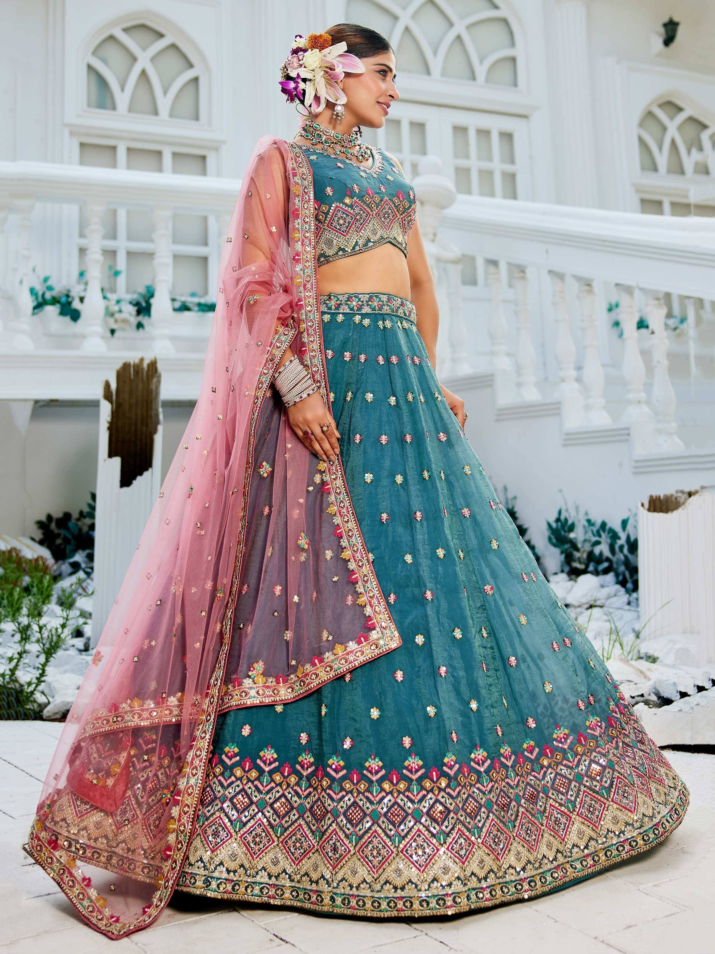 Teal embroidered lehenga choli with pink dupatta, floral hair accessory, and traditional jewelry for Indian ethnic wear.
