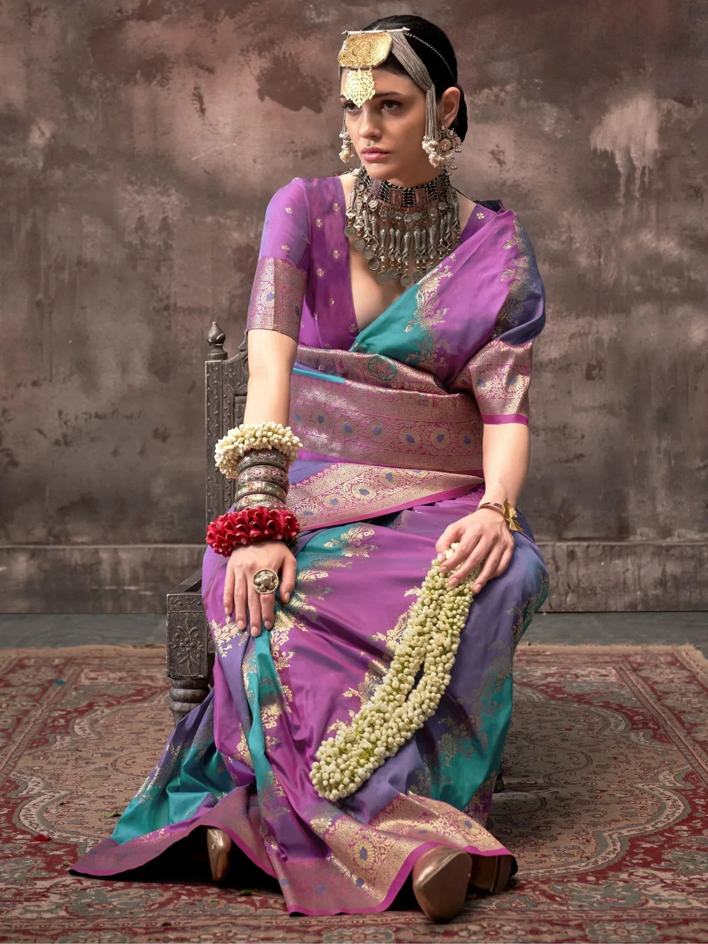 Purple and teal designer saree with gold embroidery, traditional Indian jewelry, and floral accessories