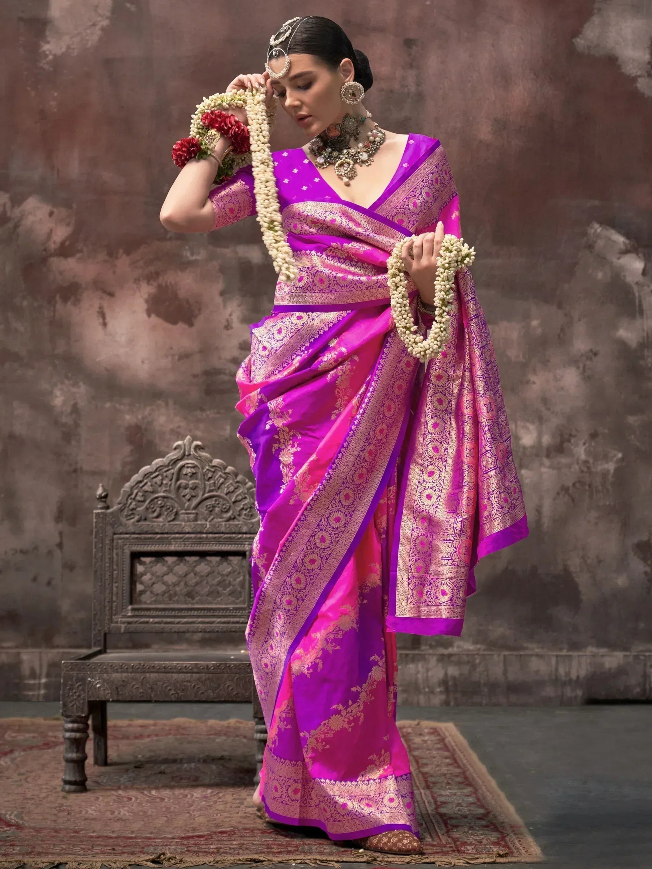 Vibrant purple and pink designer saree with gold embroidery, paired with traditional jewelry and floral garlands