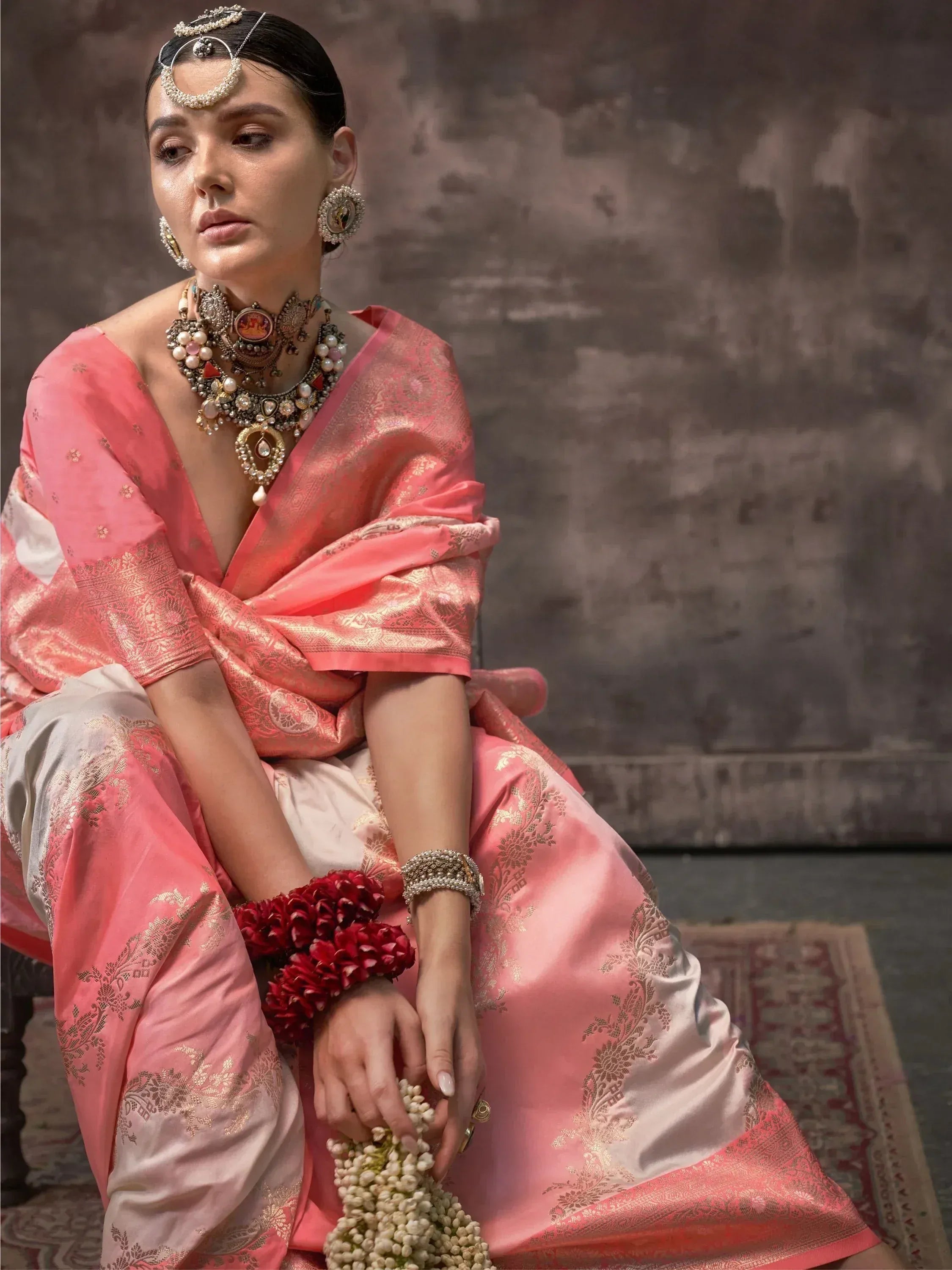 Woman in pink ethnic saree with gold embroidery, traditional jewelry, and floral accessories