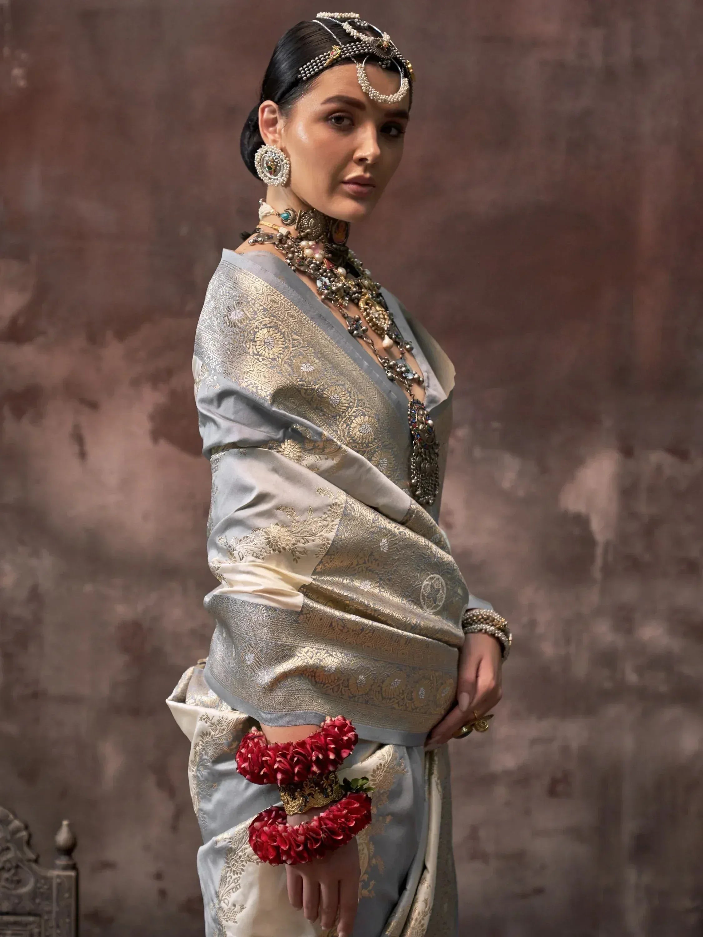 Elegant woman in silver and gold embroidered saree with traditional Indian jewelry and floral wrist adornments