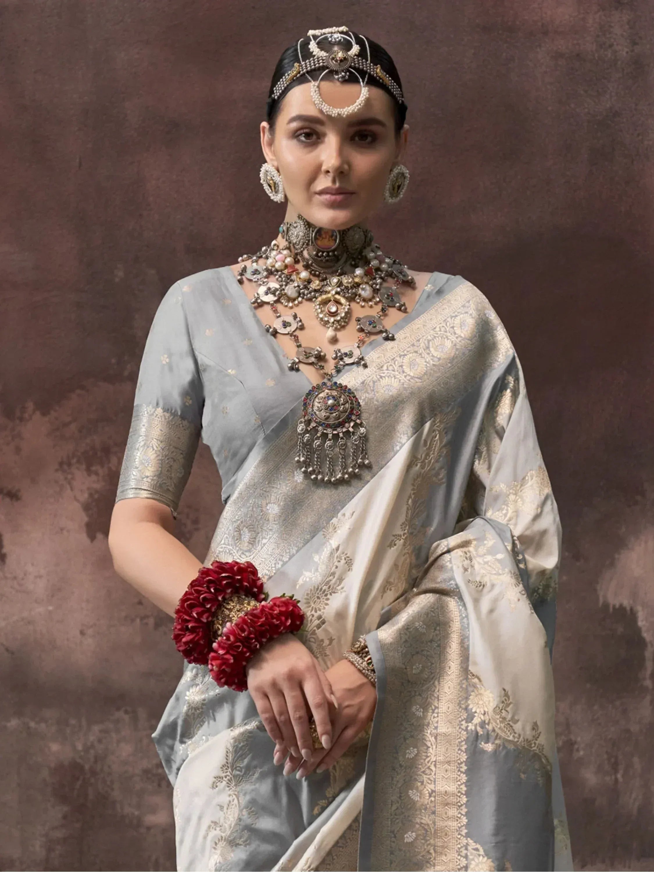 Elegant woman in light blue designer saree with gold embroidery, traditional jewelry, and red floral wristband