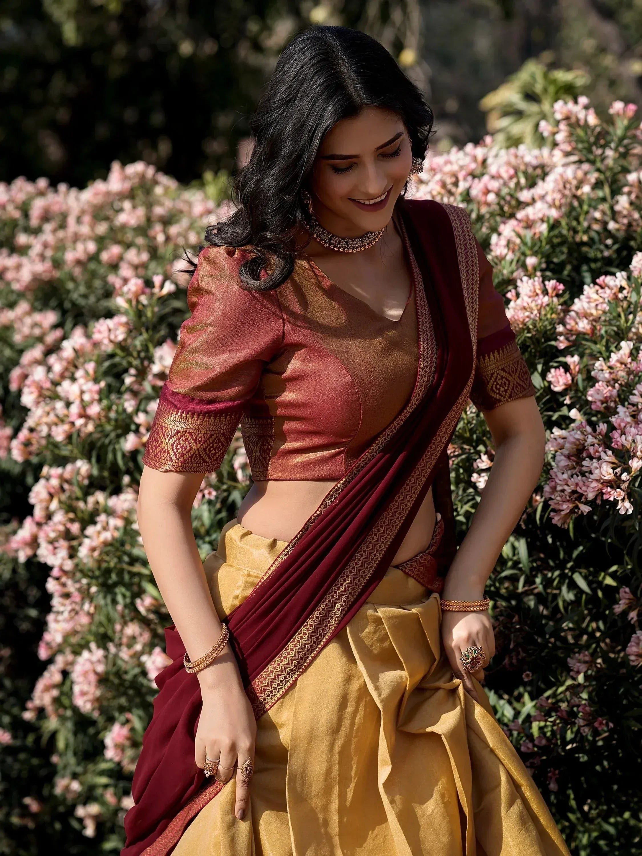 Woman in maroon and gold designer lehenga choli with floral backdrop, ethnic Indian wear