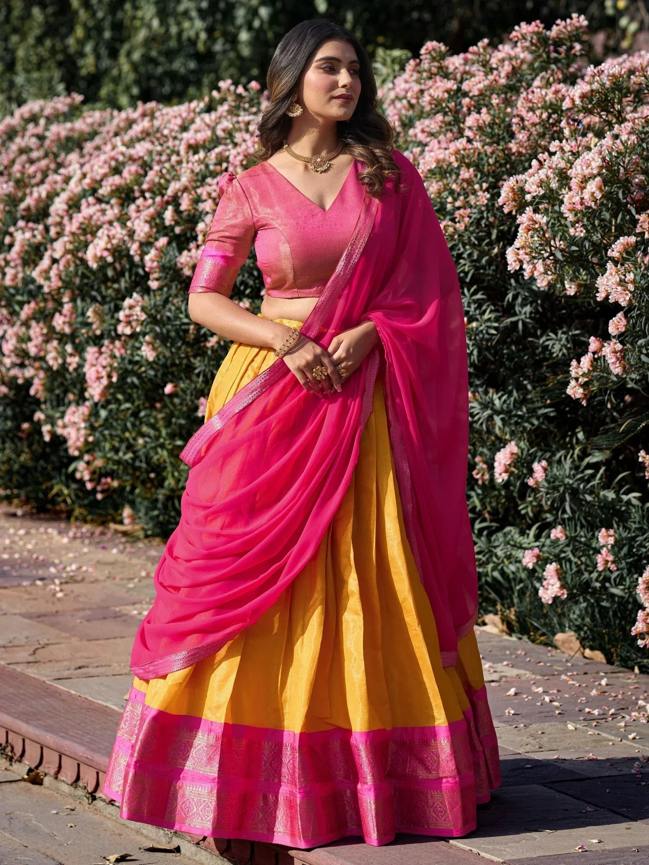 Woman in vibrant pink and yellow designer lehenga choli with floral garden backdrop