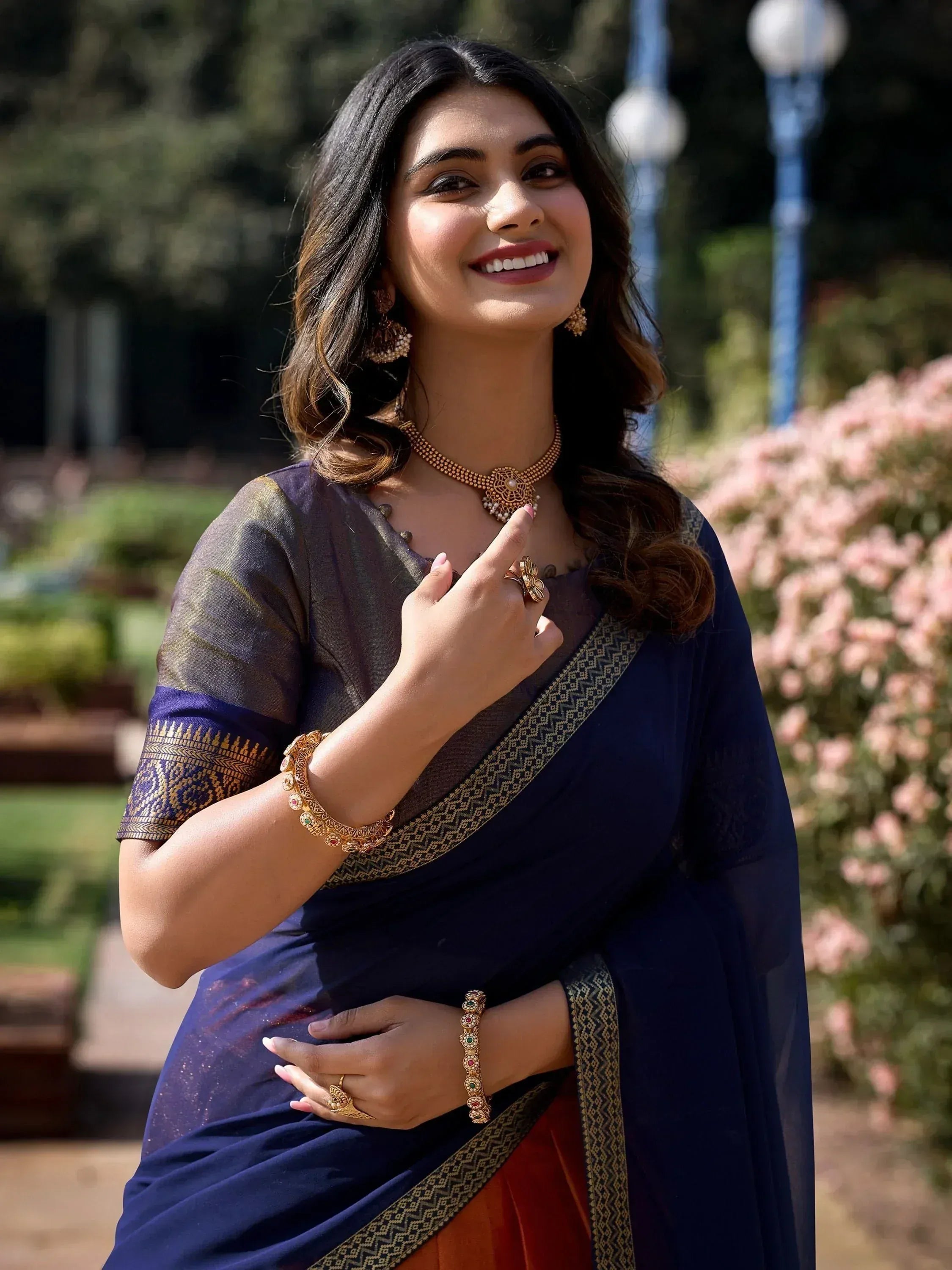 Woman in navy blue saree with gold border, traditional jewelry, smiling outdoors