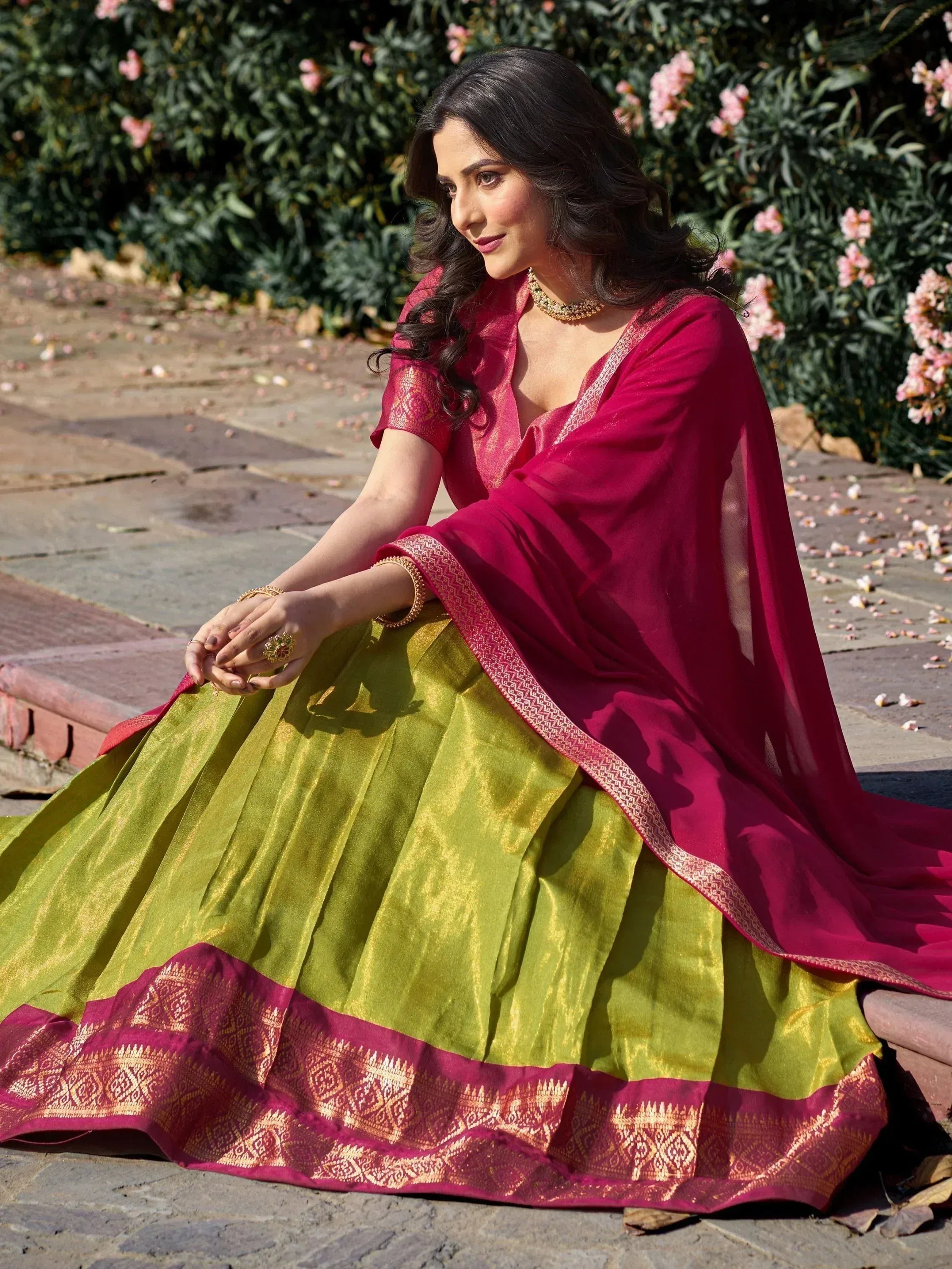 Woman in vibrant pink and green designer lehenga choli with gold embroidery, perfect for Indian ethnic occasions.