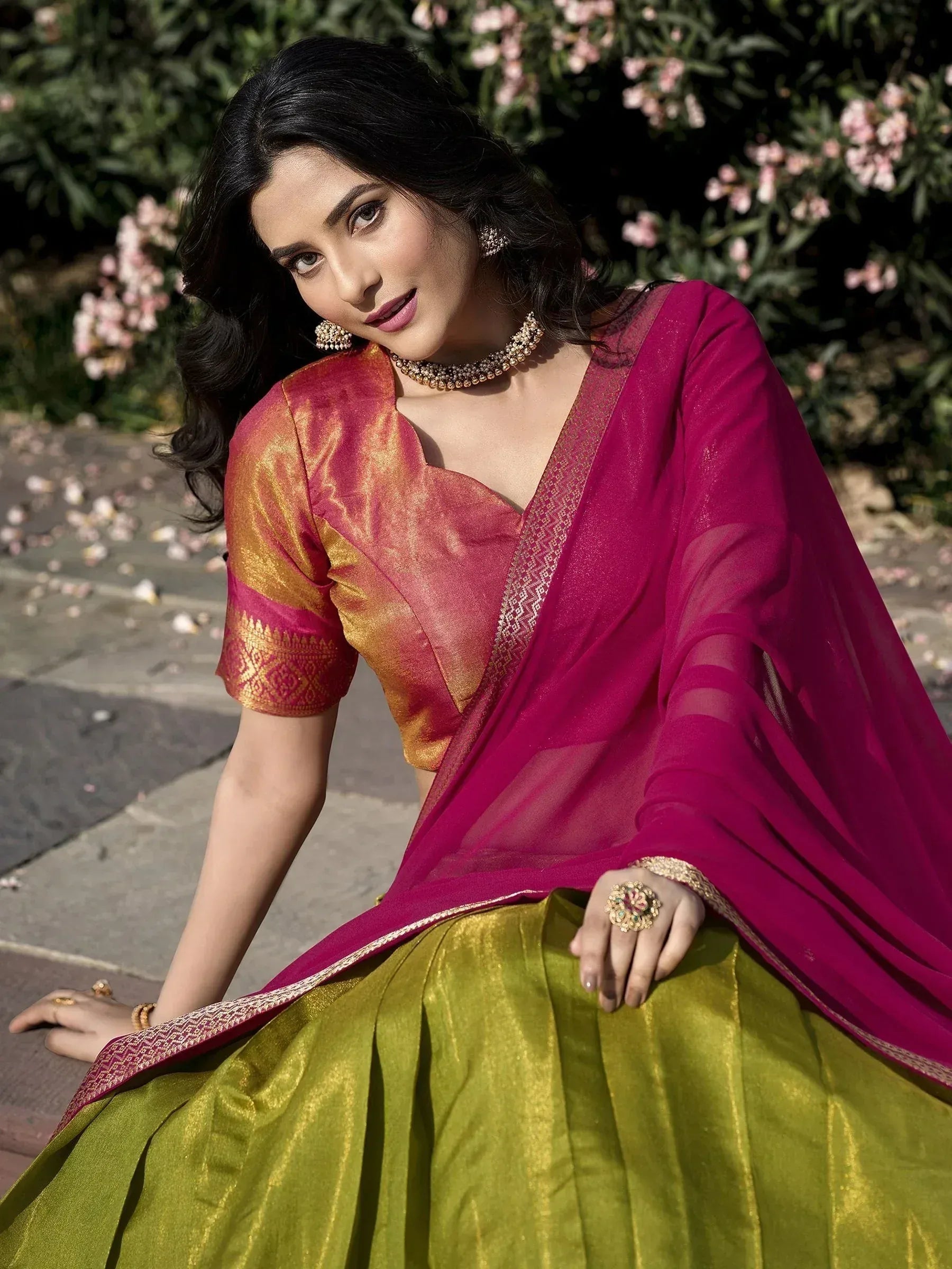 Woman in vibrant pink and green designer lehenga choli with gold embroidery, styled for ethnic occasions
