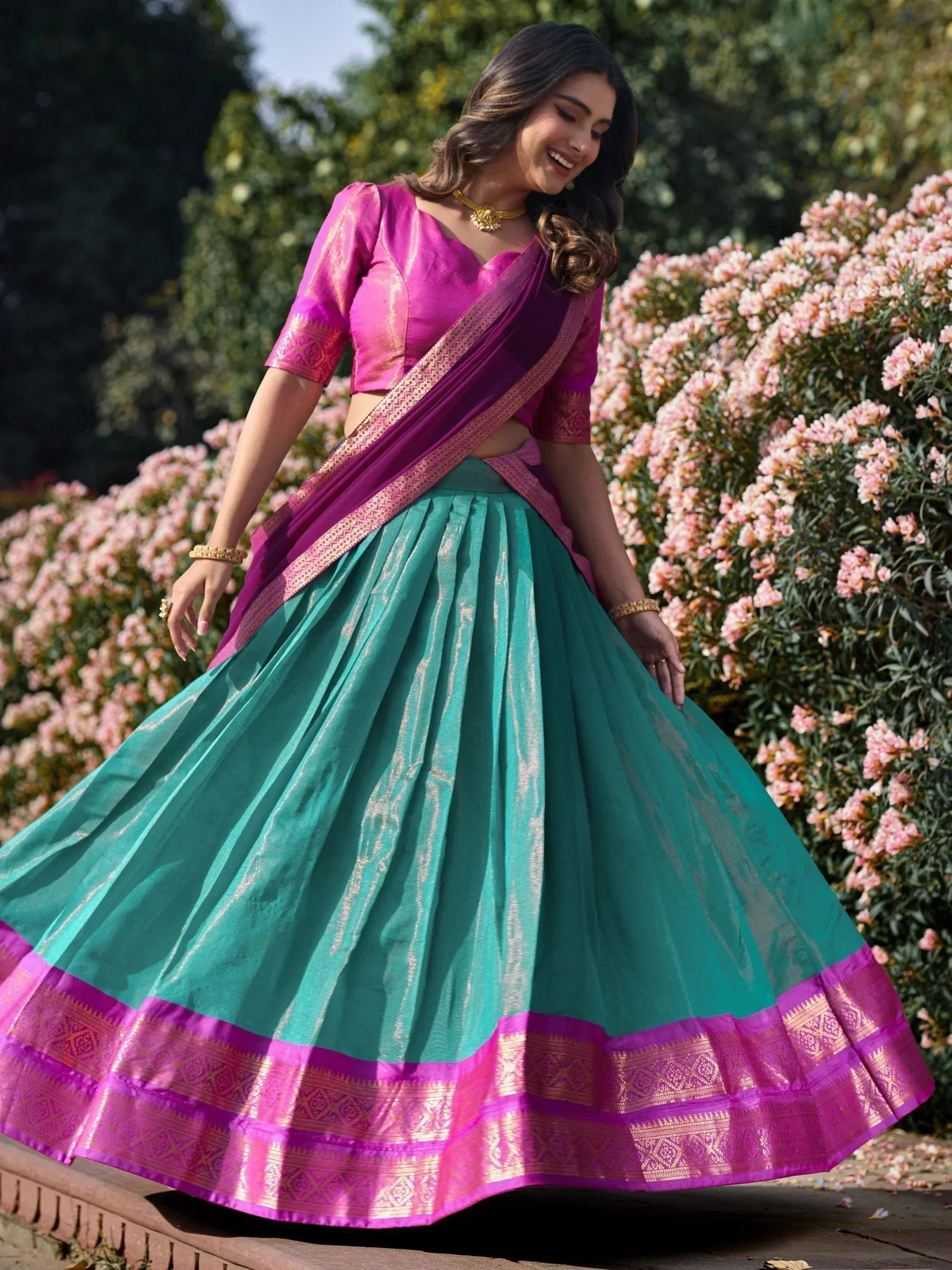 Woman in vibrant pink and teal designer lehenga choli with golden border, perfect for Indian ethnic wear occasions