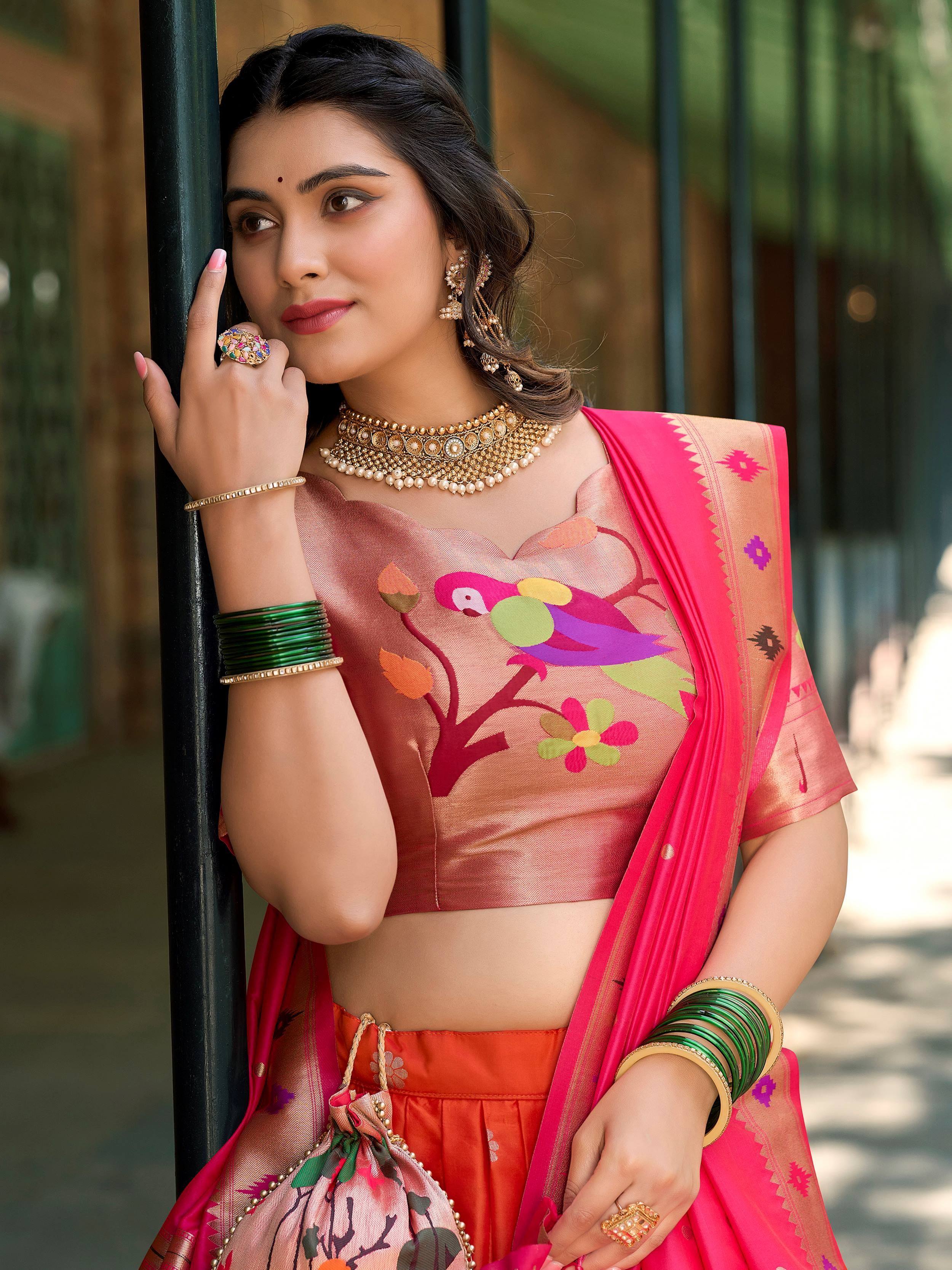 Woman in vibrant pink and orange designer lehenga choli with parrot print, paired with gold jewelry and green bangles.
