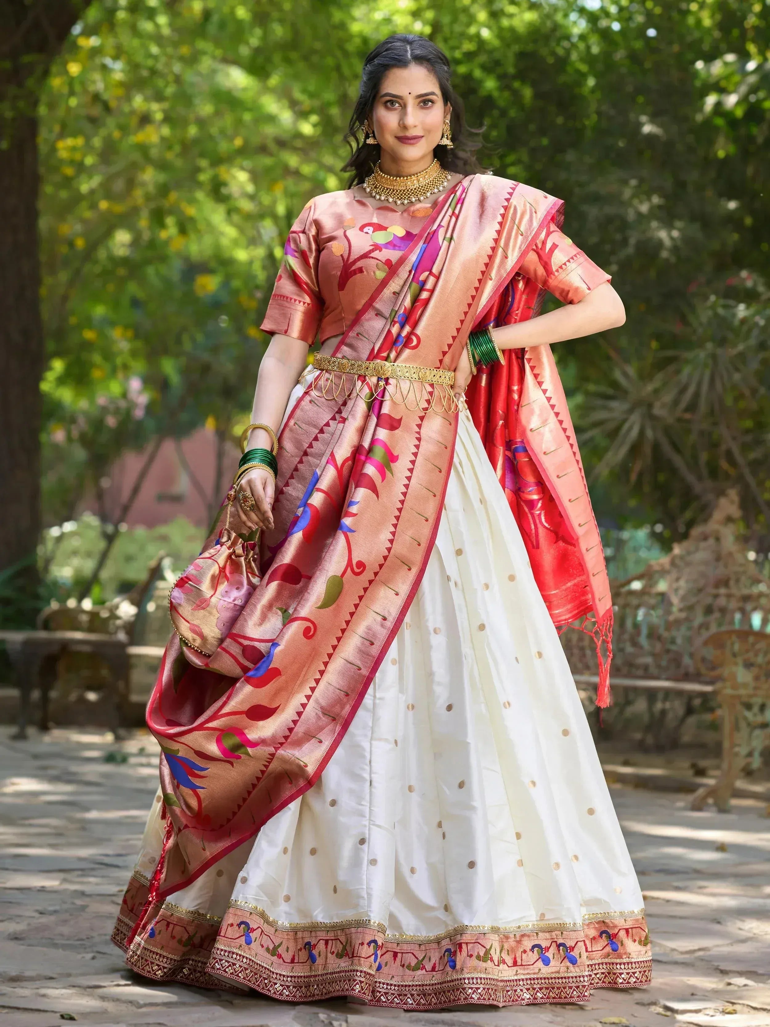 Woman in designer lehenga choli with colorful bird print, gold belt, and traditional jewelry outdoors