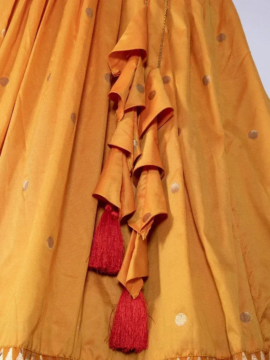 Mustard yellow ethnic lehenga with gold polka dots and red tassels, perfect for Indian weddings or festive occasions.
