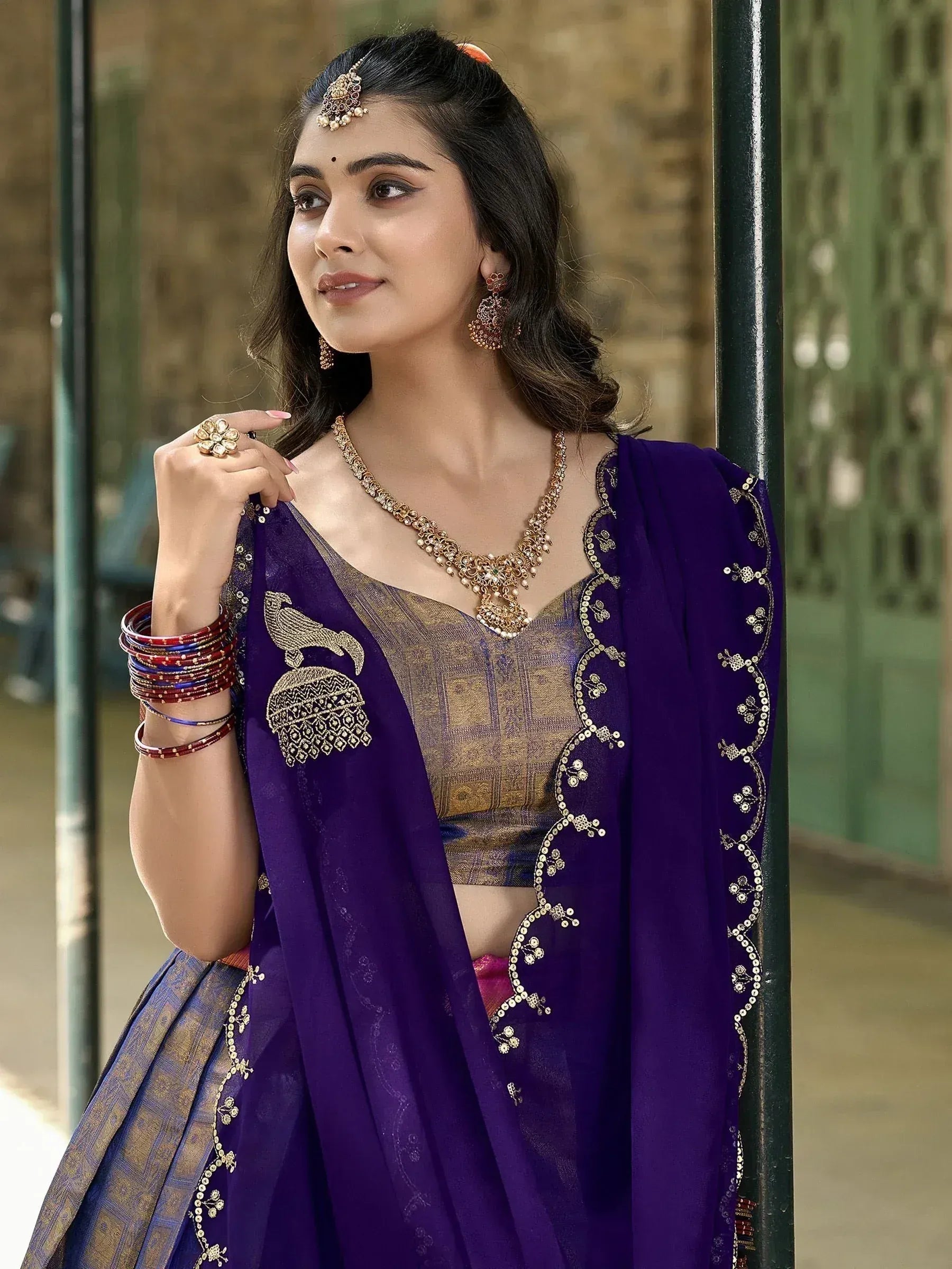 Woman in purple embroidered lehenga choli with gold jewelry, traditional Indian ethnic wear