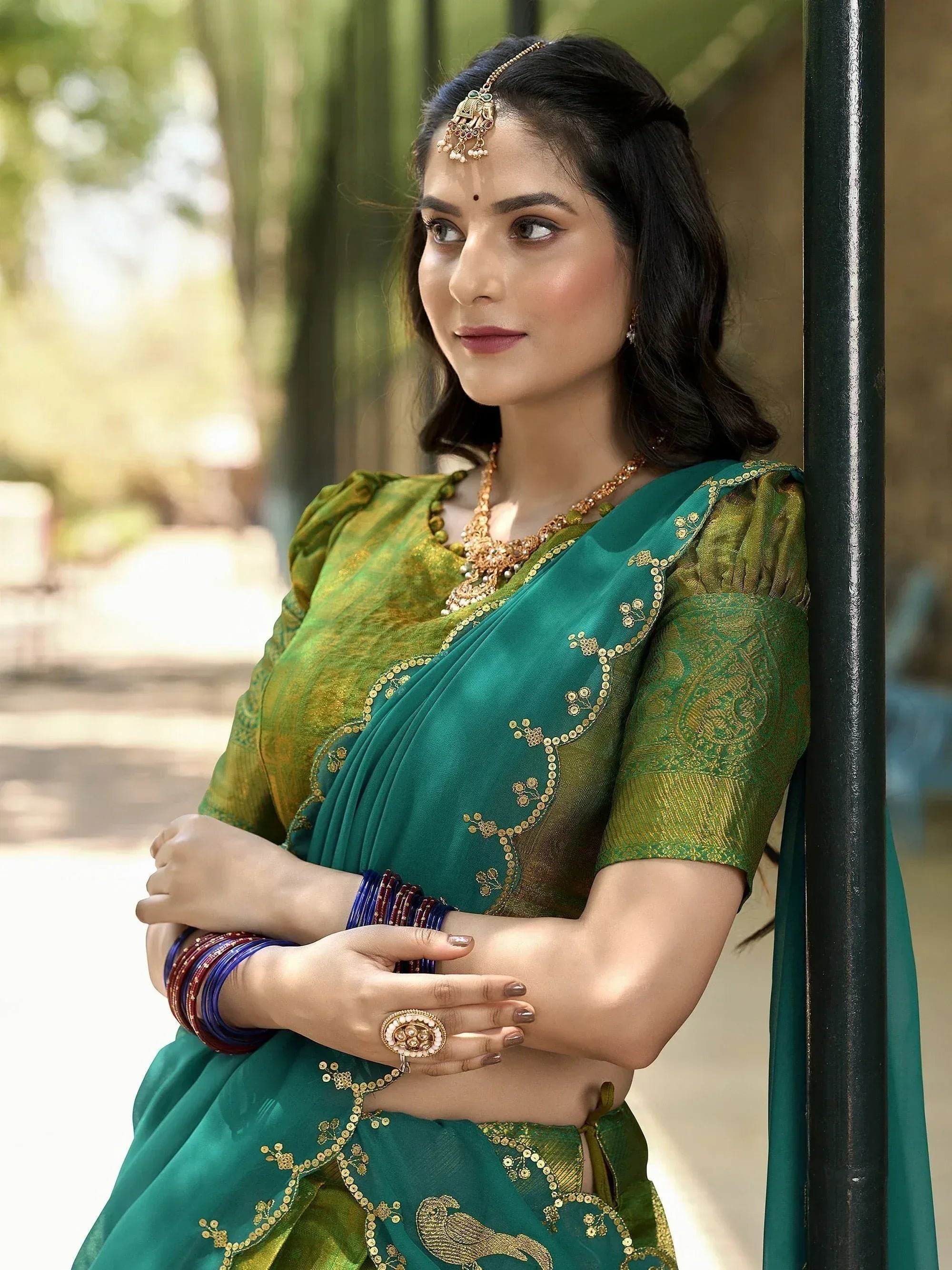 Woman in green and gold embroidered saree with traditional jewelry, perfect for Indian ethnic occasions.