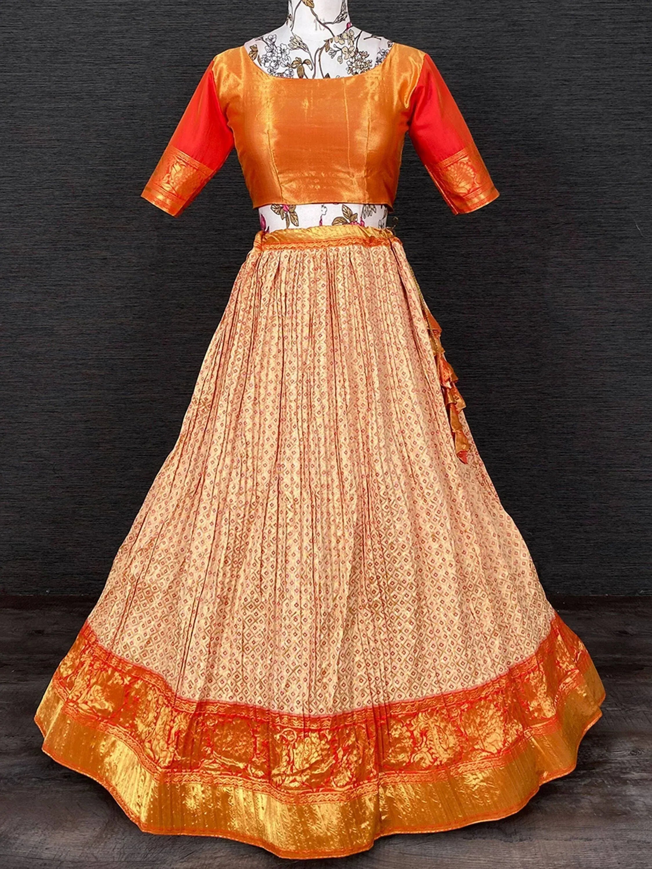Orange and red ethnic lehenga choli with patterned skirt and gold border, perfect for Indian festivals and weddings